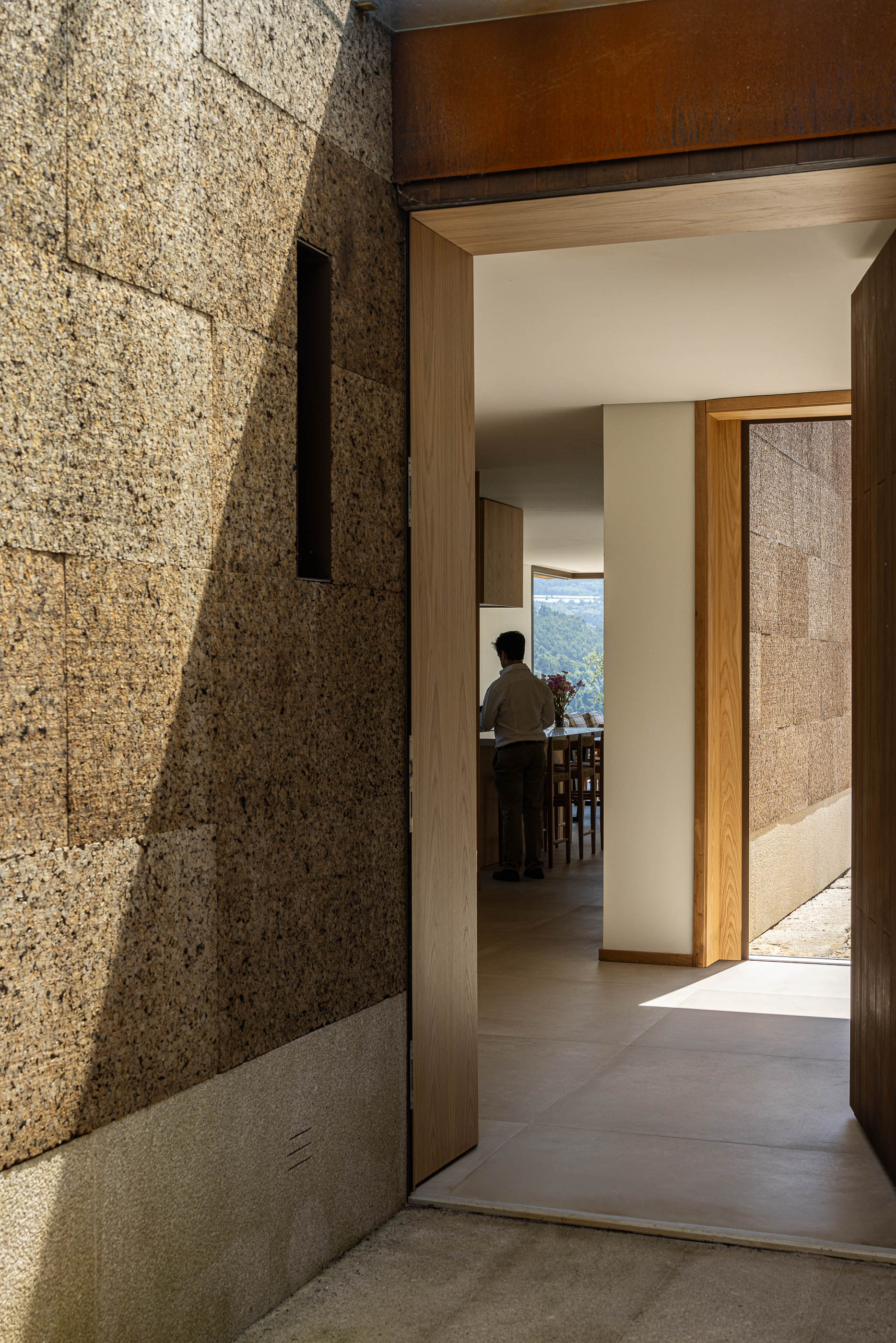 Exterior: Detalhe da parede em cortiça, porta em madeira e vista para a cozinha. — Casa da Levada arquitetura Tsou Arquitectos em Penafiel