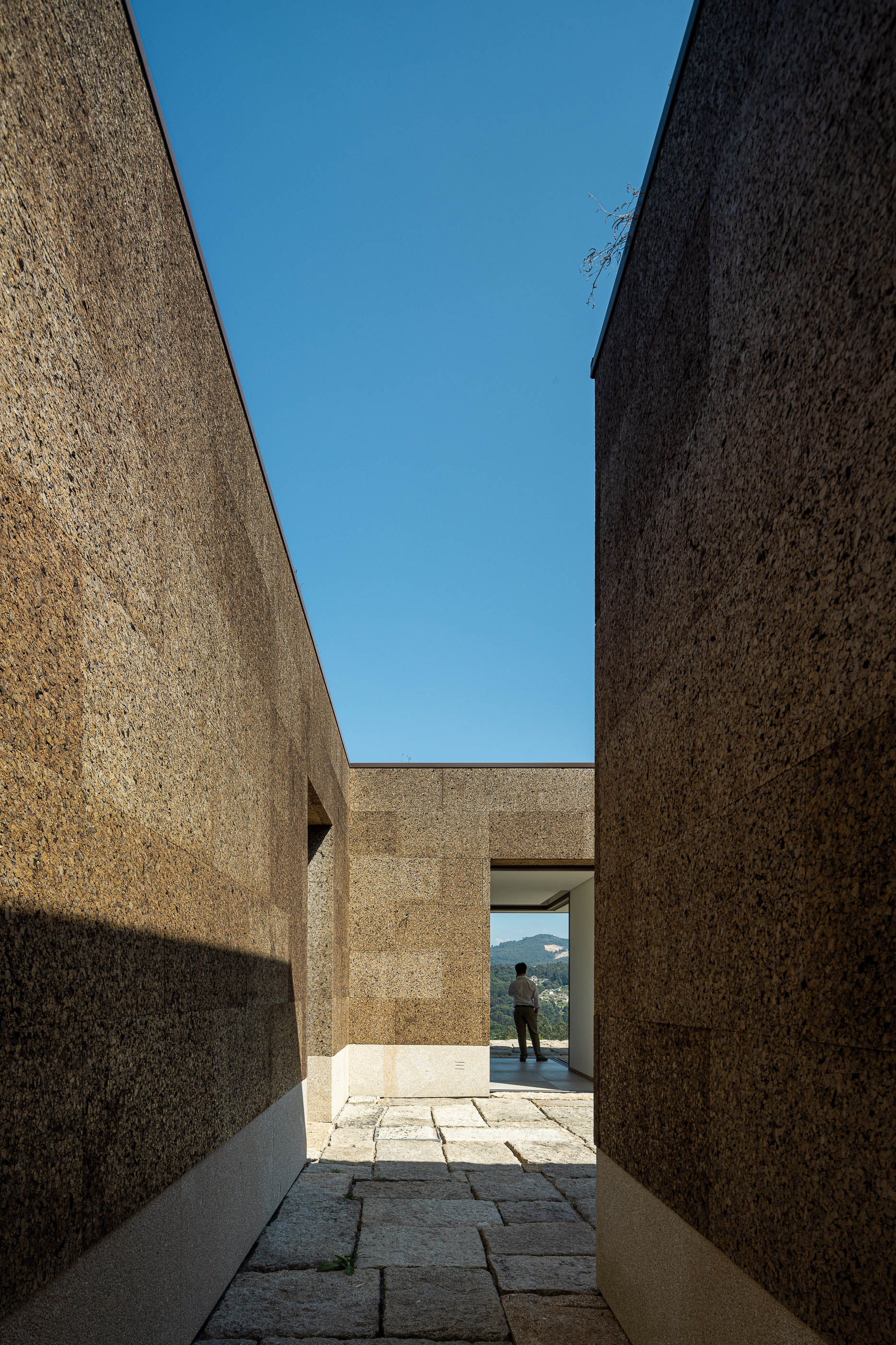 Exterior: Passadiço entre paredes em cortiça, com pavimento em pedra e vista para o interior. — Casa da Levada arquitetura Tsou Arquitectos em Penafiel