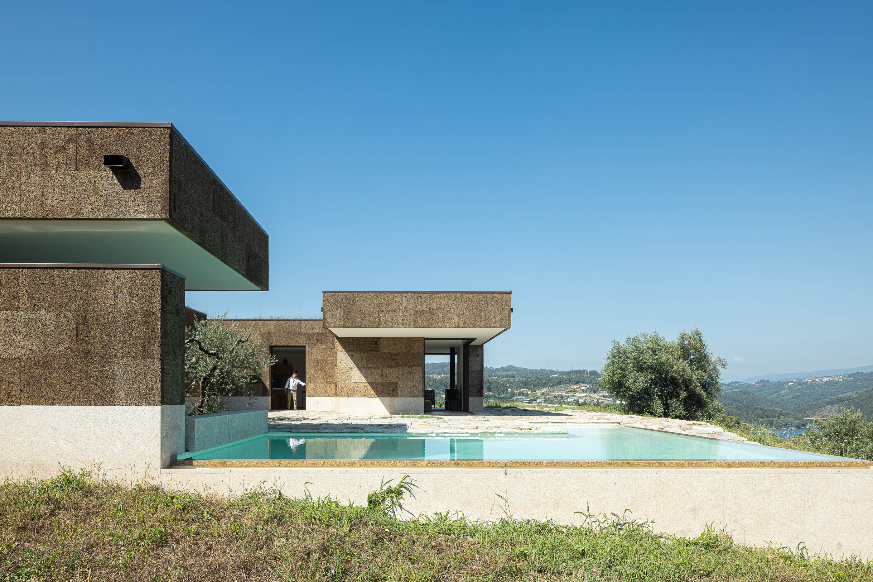 Exterior: Piscina com borda infinita, pátio em pedra e fachada revestida em cortiça. — Casa da Levada arquitetura Tsou Arquitectos em Penafiel