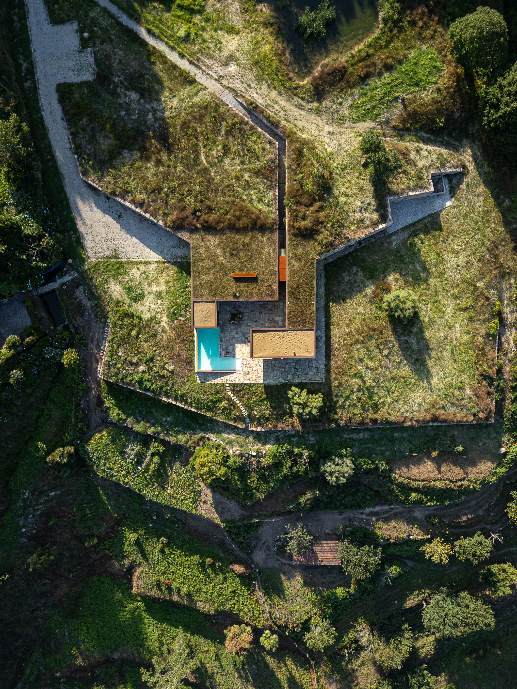 Exterior: Vista aérea da casa com telhado verde, piscina e pátio em pedra. — Casa da Levada arquitetura Tsou Arquitectos em Penafiel