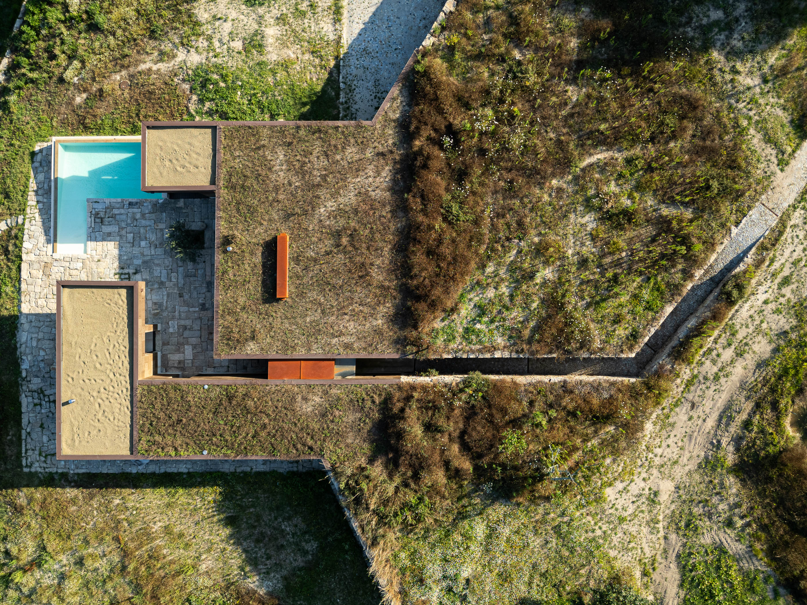 Exterior: Vista aérea da casa com telhado verde, piscina e pátio em pedra. — Casa da Levada arquitetura Tsou Arquitectos em Penafiel
