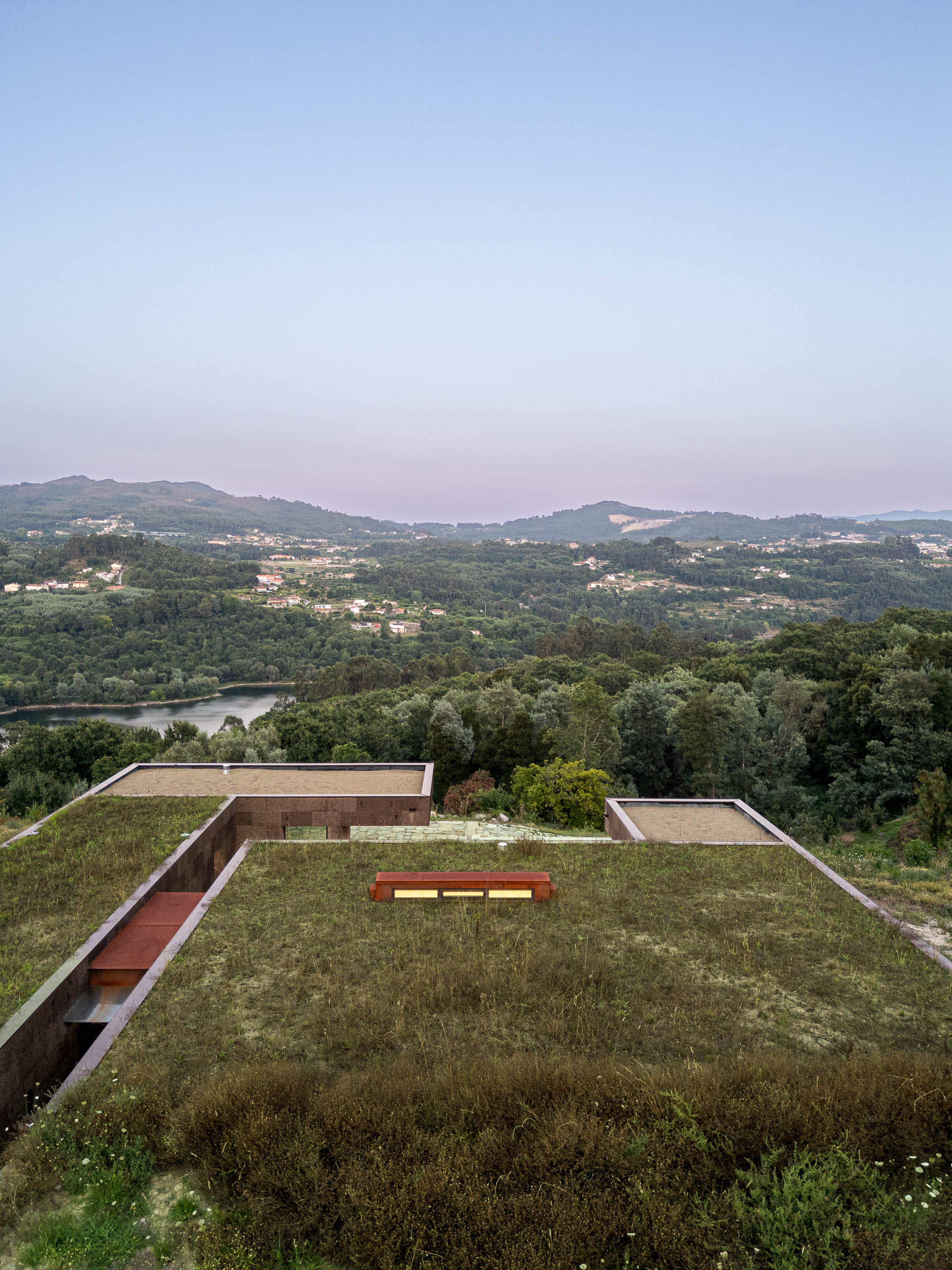 Exterior: Vista aérea da casa com telhado verde e paisagem natural. — Casa da Levada arquitetura Tsou Arquitectos em Penafiel
