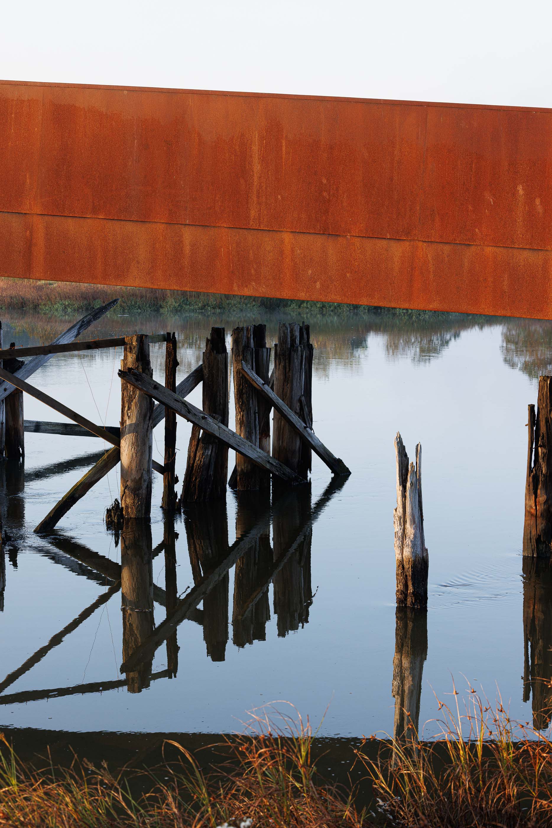 Ponte: Detalhe dos pilares de madeira da antiga ponte, contrastando com a estrutura em aço corten. — Requalificação da antiga Ponte da Fareja arquitetura Rómulo Neto Arquitectos em Aveiro