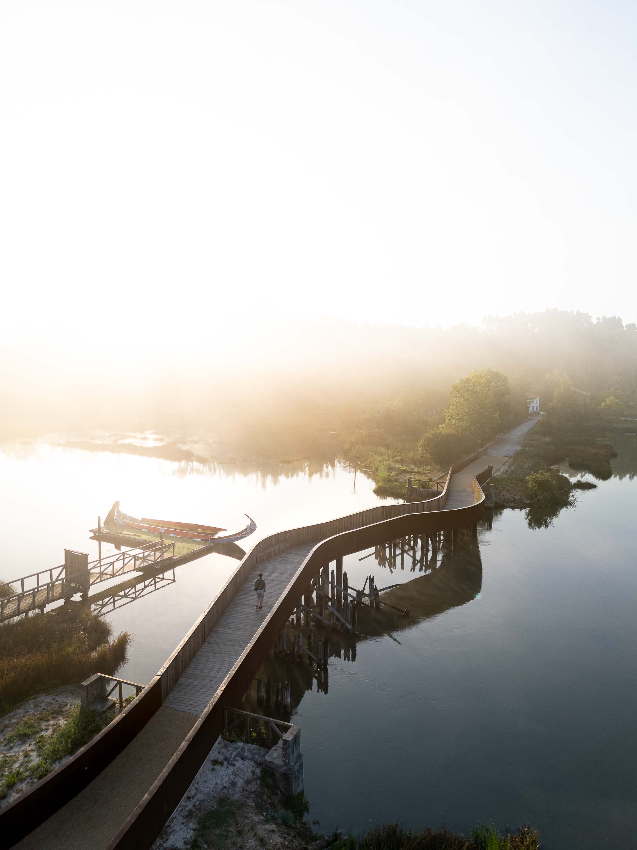 Ponte: Vista aérea da ponte com passadiço de madeira, ligando a margem a um cais com barco moliceiro. — Requalificação da antiga Ponte da Fareja arquitetura Rómulo Neto Arquitectos em Aveiro