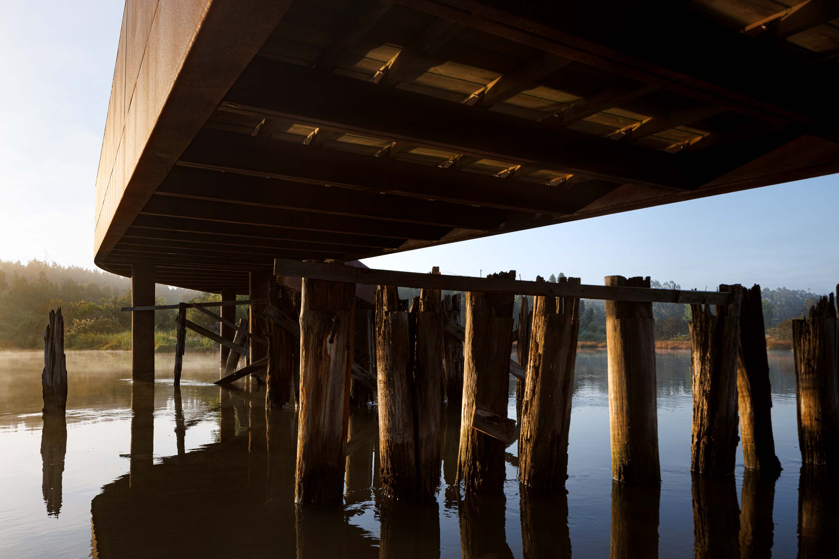 Ponte: Vista inferior da ponte, mostrando a estrutura de suporte em aço e os pilares de madeira. — Requalificação da antiga Ponte da Fareja arquitetura Rómulo Neto Arquitectos em Aveiro