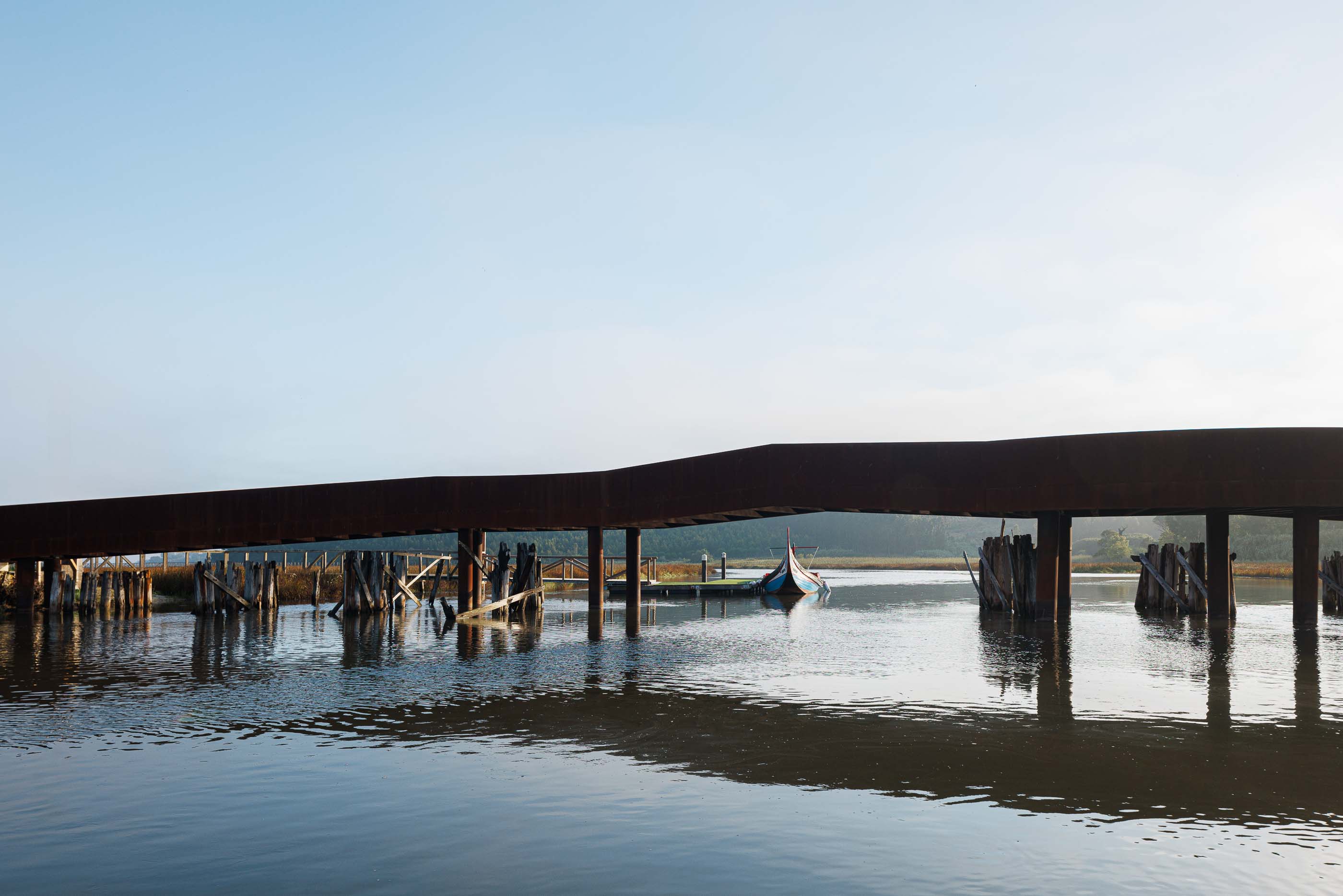 Ponte: Barco moliceiro atracado junto à ponte, com passadiço de madeira e pilares em aço corten. — Requalificação da antiga Ponte da Fareja arquitetura Rómulo Neto Arquitectos em Aveiro