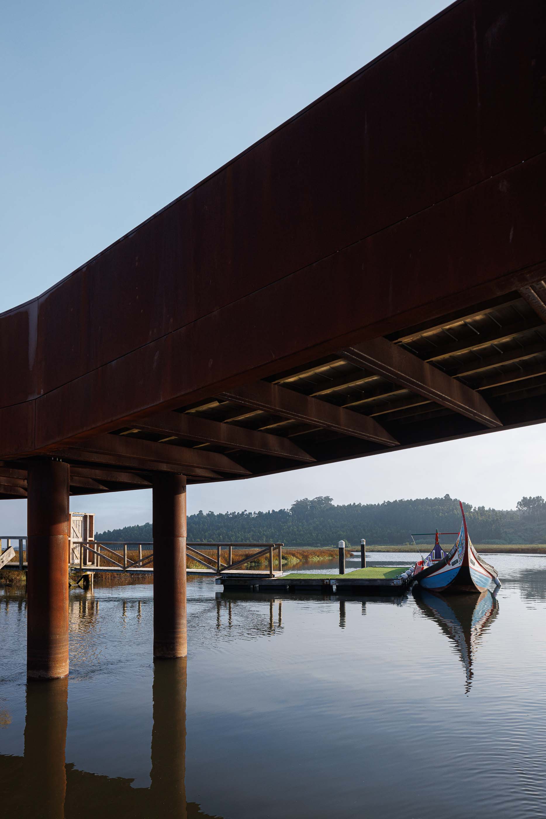 Ponte: Detalhe da estrutura inferior da ponte, com pilares de madeira e aço corten. — Requalificação da antiga Ponte da Fareja arquitetura Rómulo Neto Arquitectos em Aveiro