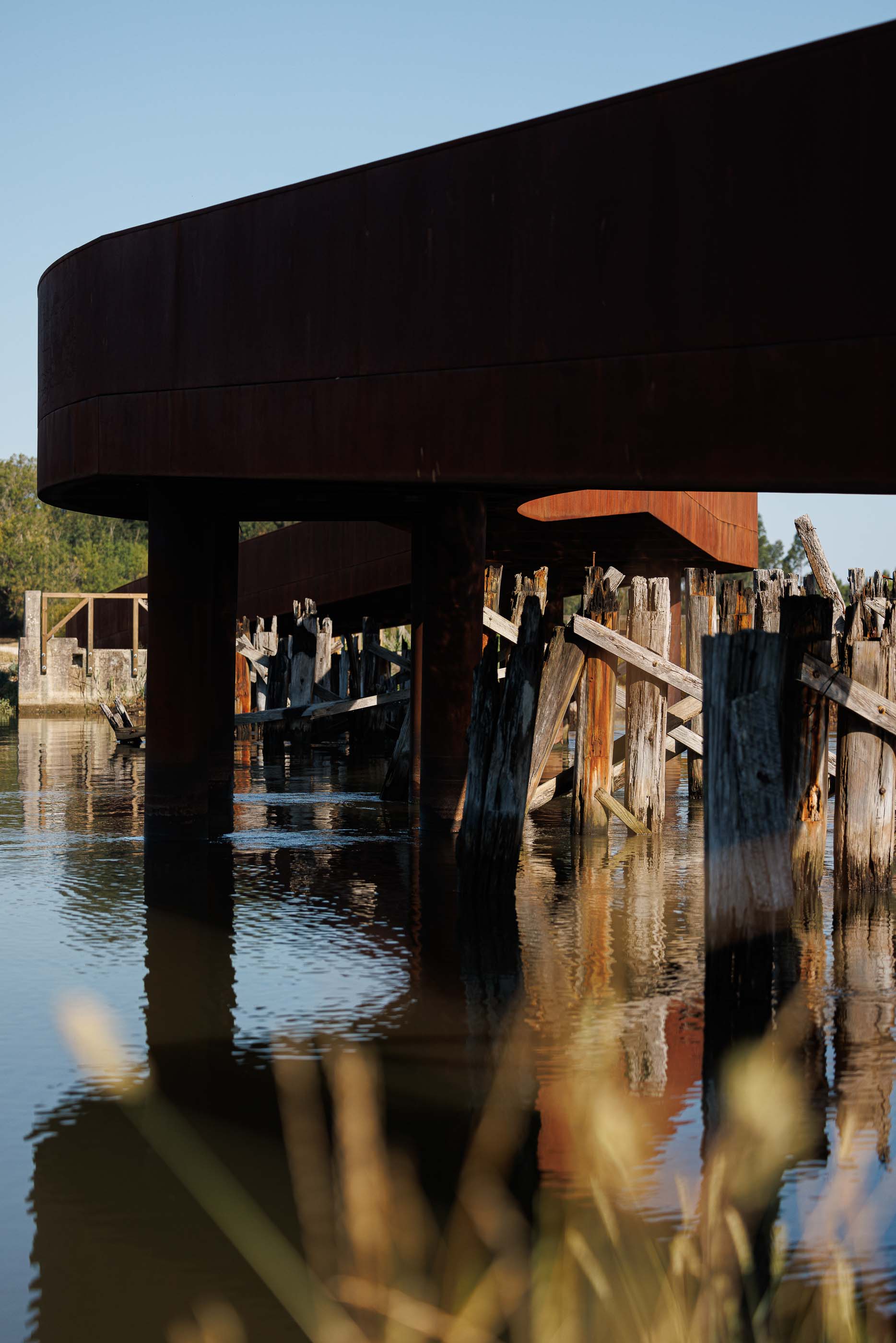 Ponte: Detalhe da estrutura inferior da ponte, com vigas de madeira e aço corten. — Requalificação da antiga Ponte da Fareja arquitetura Rómulo Neto Arquitectos em Aveiro