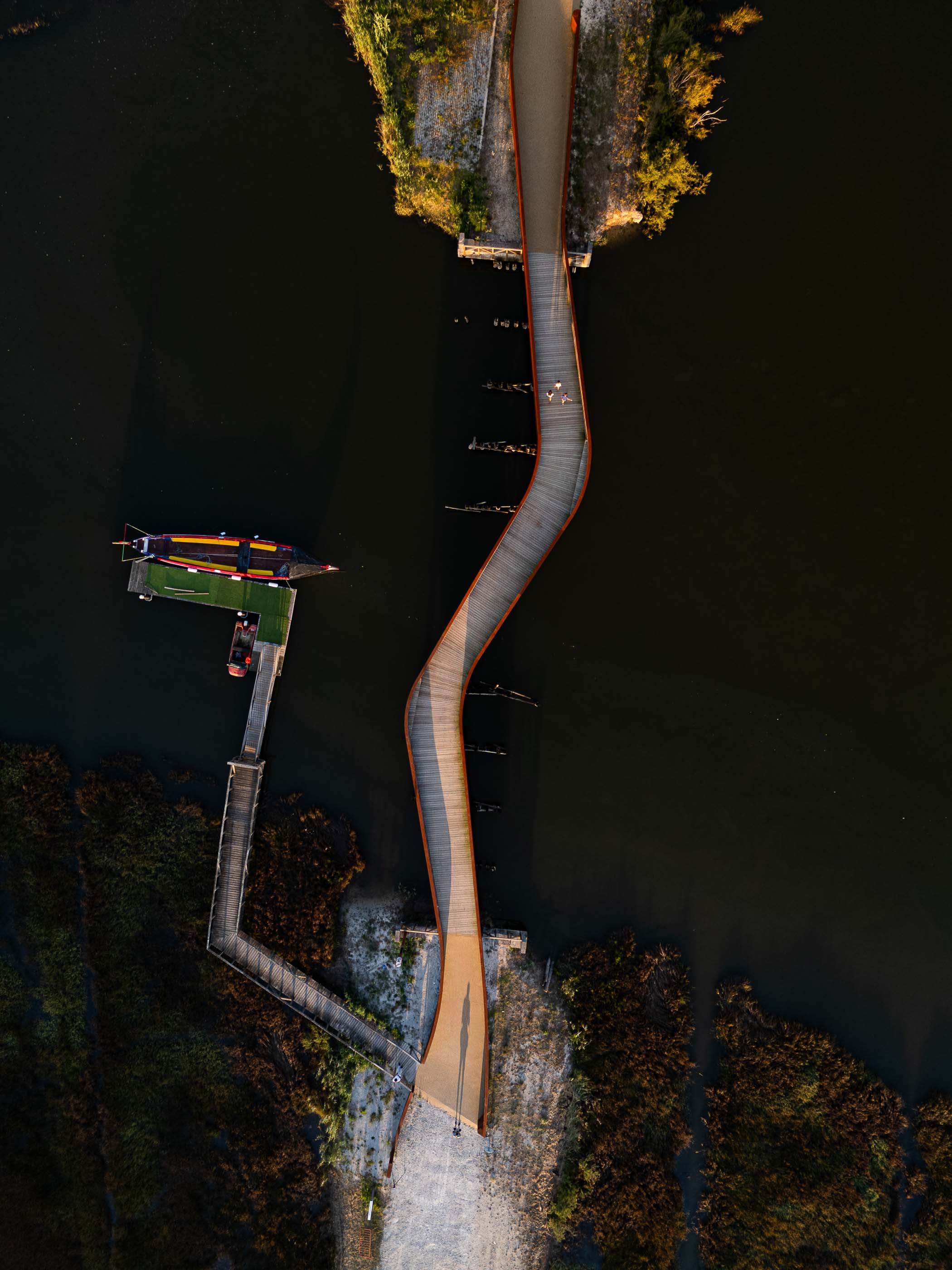 Ponte: Vista aérea noturna da ponte iluminada, com passadiço em madeira e estrutura em aço corten. — Requalificação da antiga Ponte da Fareja arquitetura Rómulo Neto Arquitectos em Aveiro