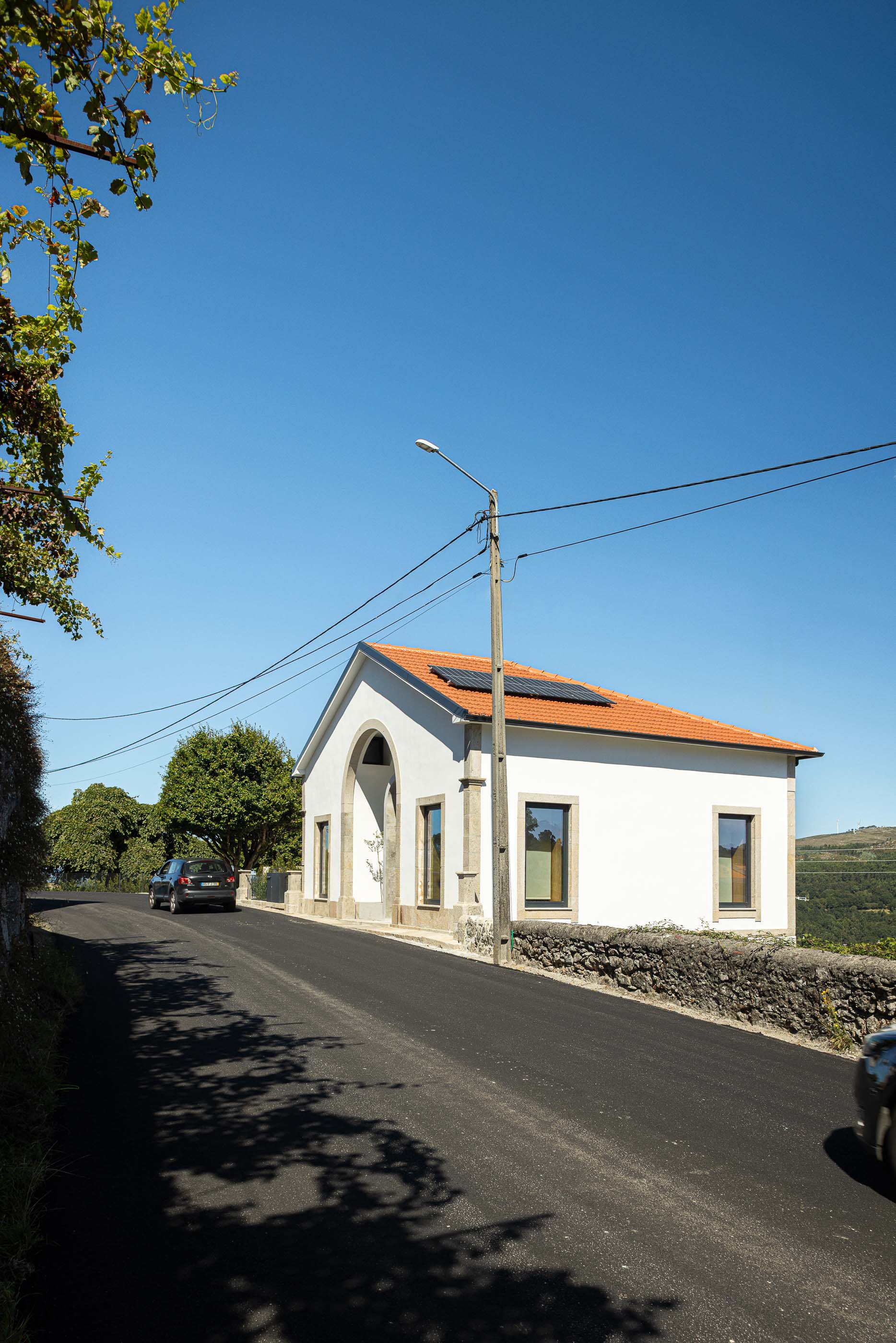 Fachada: Casa branca com telhado de telha, arco em pedra e painéis solares, vista da rua. — Casa Arco arquitetura Tiago Sousa Arquitecto em Paredes de Coura