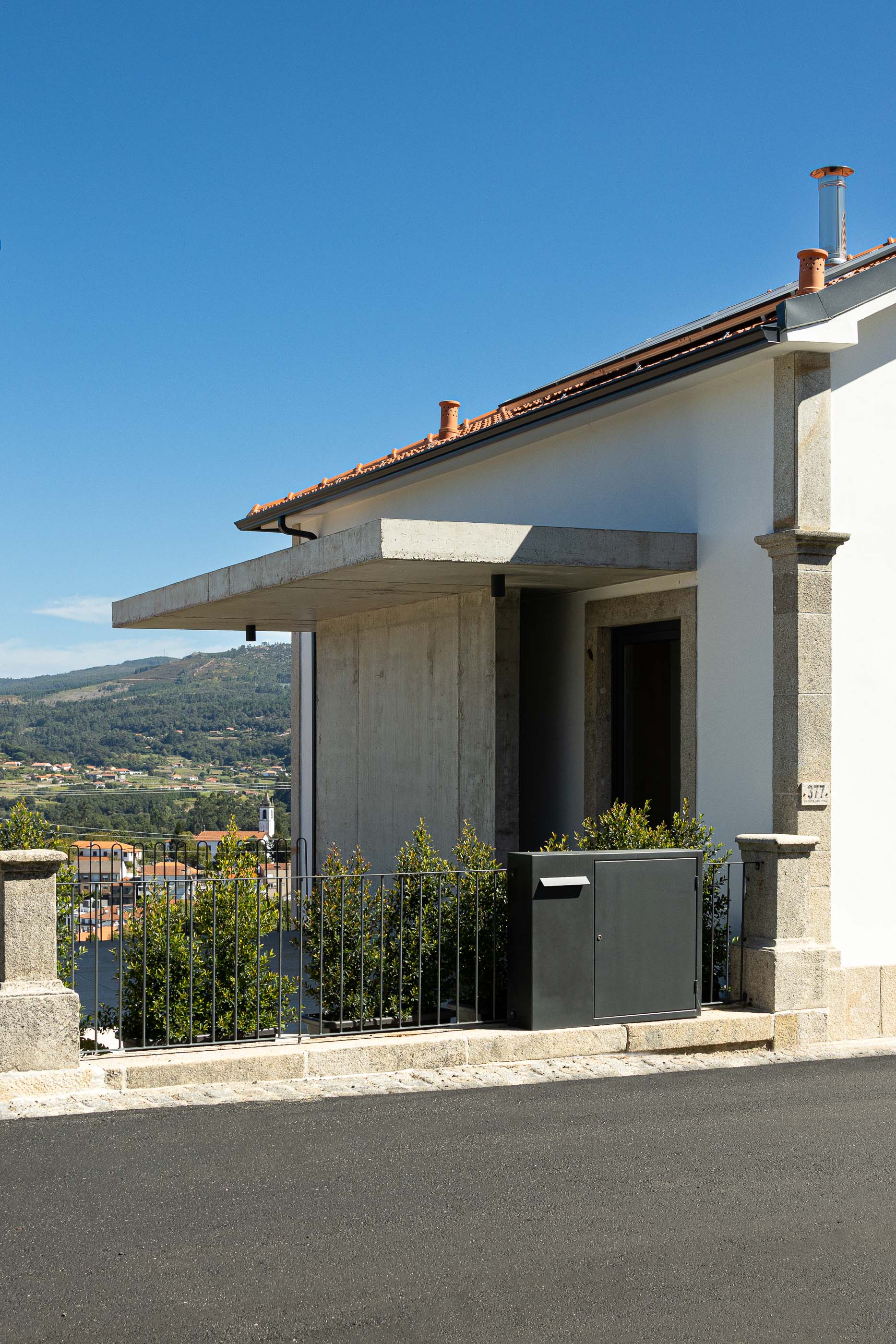Entrada: Detalhe da entrada com alpendre em betão, caixote do correio cinzento e paisagem montanhosa. — Casa Arco arquitetura Tiago Sousa Arquitecto em Paredes de Coura