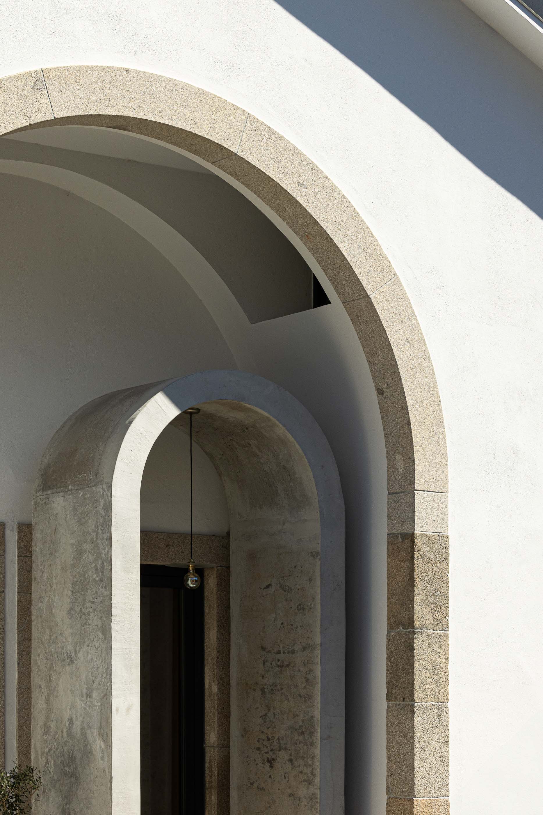 Entrada: Detalhe da entrada principal com arcos em pedra, candeeiro suspenso e porta escura. — Casa Arco arquitetura Tiago Sousa Arquitecto em Paredes de Coura