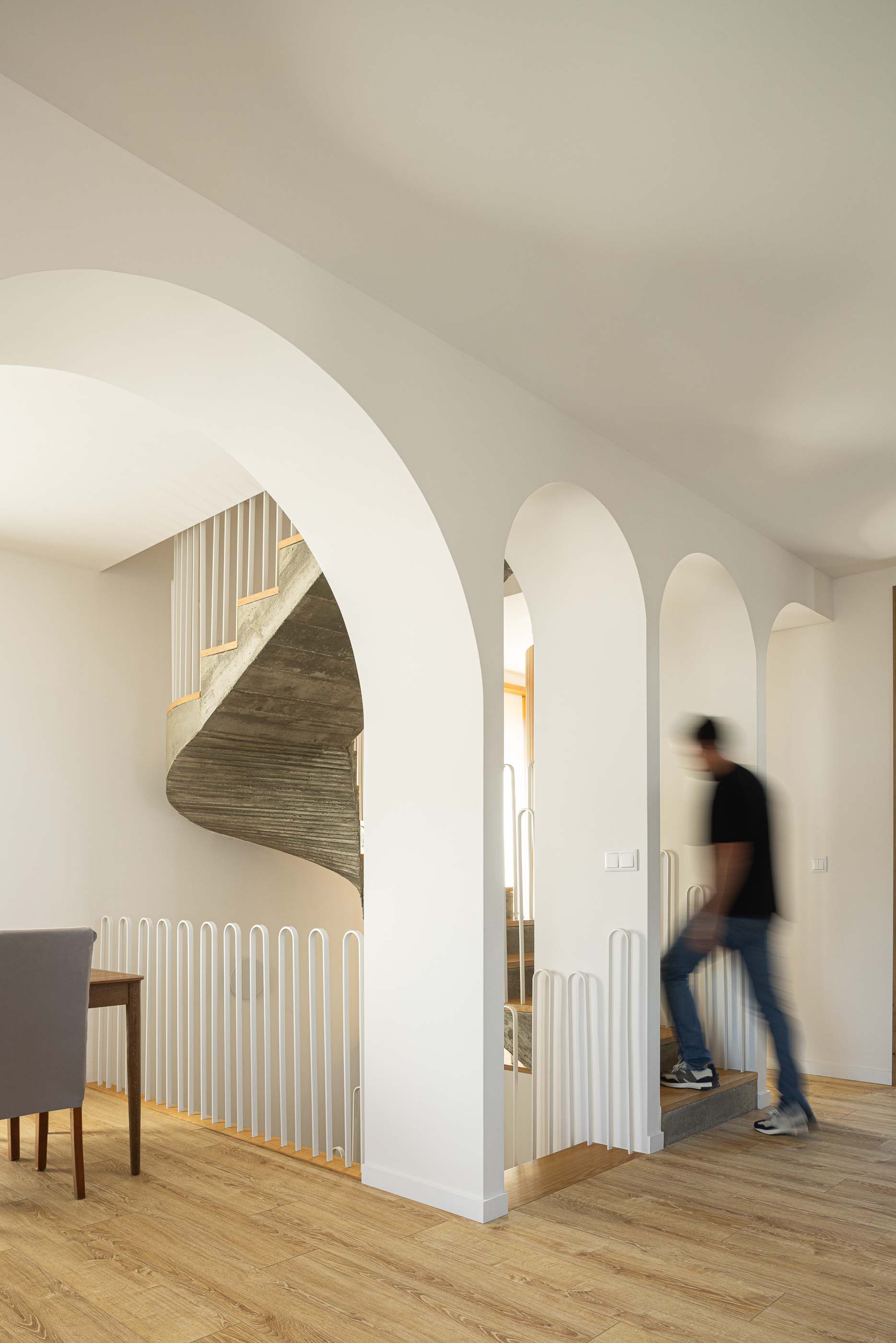 Hall: Arcos interiores em branco, escada em betão e madeira, guarda em metal branco. — Casa Arco arquitetura Tiago Sousa Arquitecto em Paredes de Coura