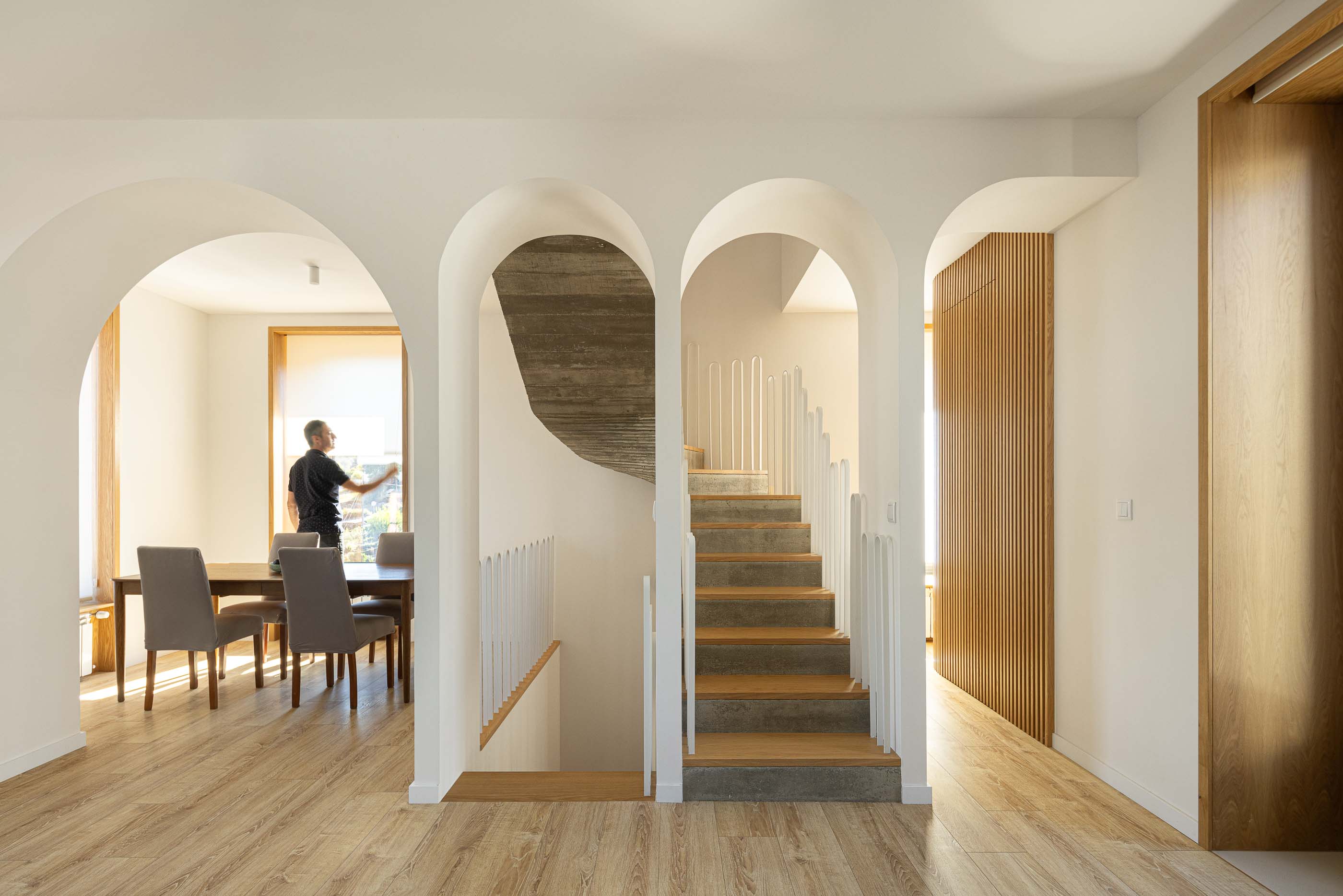 Hall: Vista do hall com arcos, escada, sala de jantar e armário em madeira. — Casa Arco arquitetura Tiago Sousa Arquitecto em Paredes de Coura