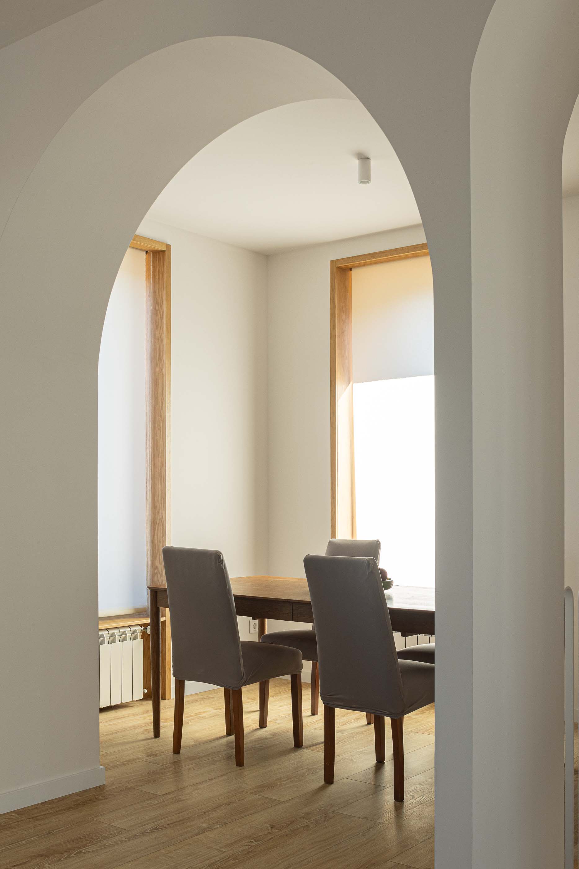 Sala de jantar: Vista da sala de jantar através de um arco, mesa em madeira e cadeiras cinzentas. — Casa Arco arquitetura Tiago Sousa Arquitecto em Paredes de Coura