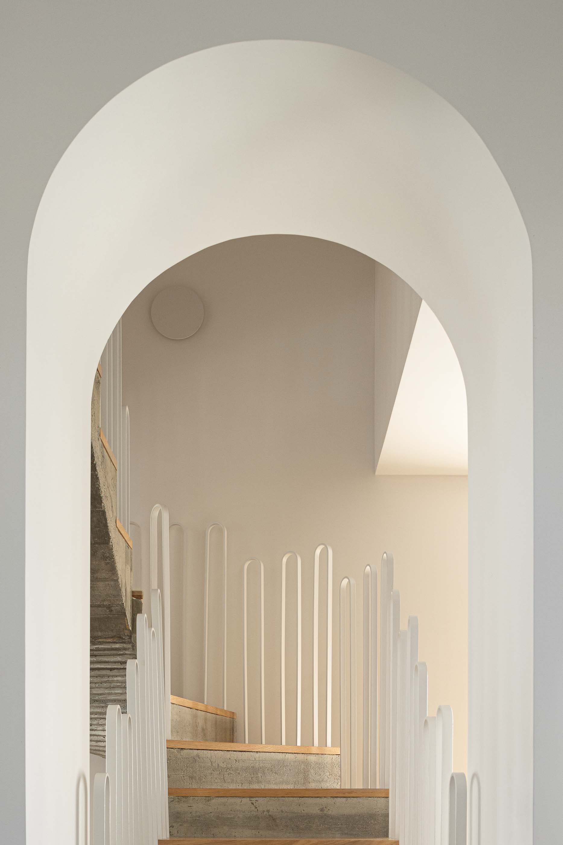 Escada: Vista da escada em betão e madeira através de um arco, com guarda em metal branco. — Casa Arco arquitetura Tiago Sousa Arquitecto em Paredes de Coura