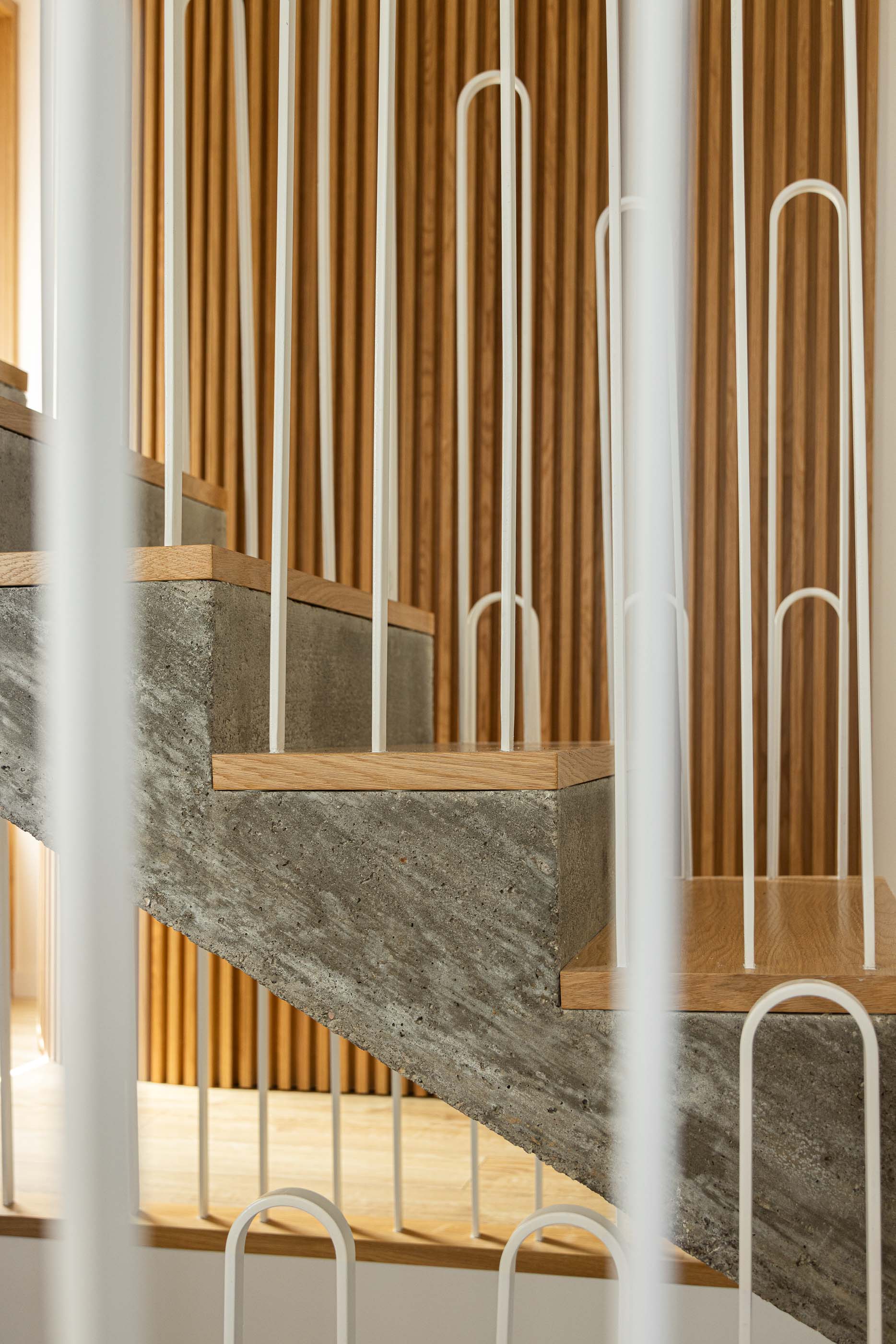Escada: Pormenor da escada com degraus em betão e madeira, guarda em metal branco e lambrim em madeira. — Casa Arco arquitetura Tiago Sousa Arquitecto em Paredes de Coura