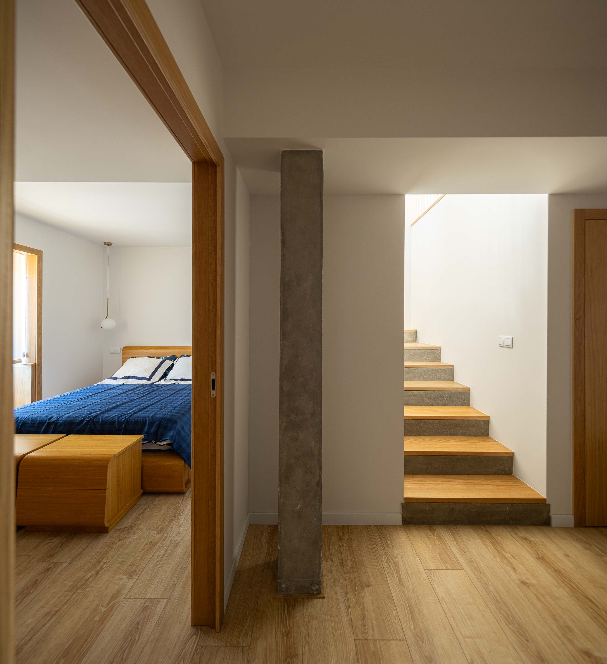 Quarto: Vista do quarto com cama de casal, roupa de cama azul e candeeiro suspenso. — Casa Arco arquitetura Tiago Sousa Arquitecto em Paredes de Coura