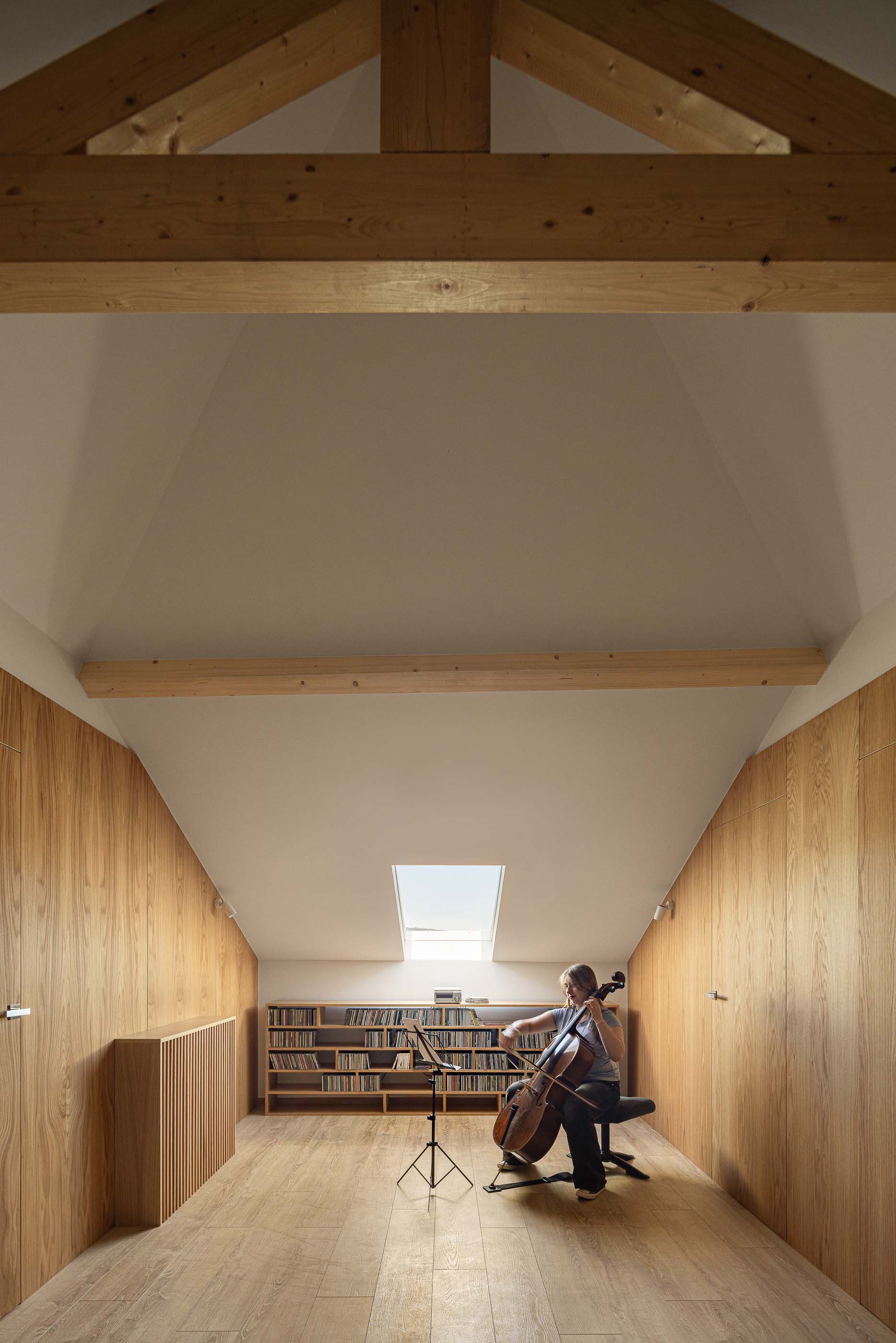 Sótão: Sótão com vigas de madeira, lambrim em madeira e estante com livros. — Casa Arco arquitetura Tiago Sousa Arquitecto em Paredes de Coura