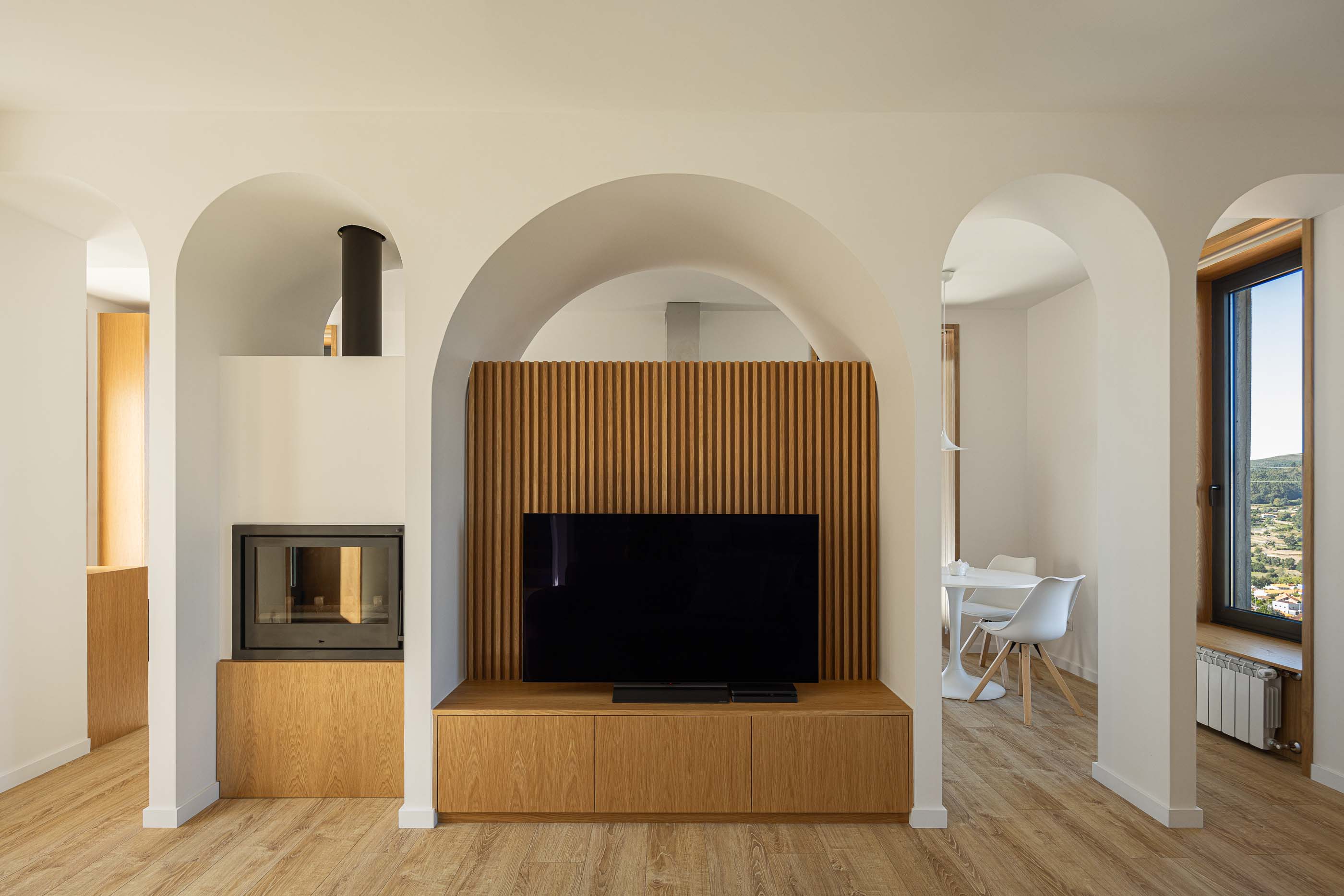 Sala de estar: Sala de estar com arcos, lareira, móvel de TV em madeira e vista para a sala de jantar. — Casa Arco arquitetura Tiago Sousa Arquitecto em Paredes de Coura