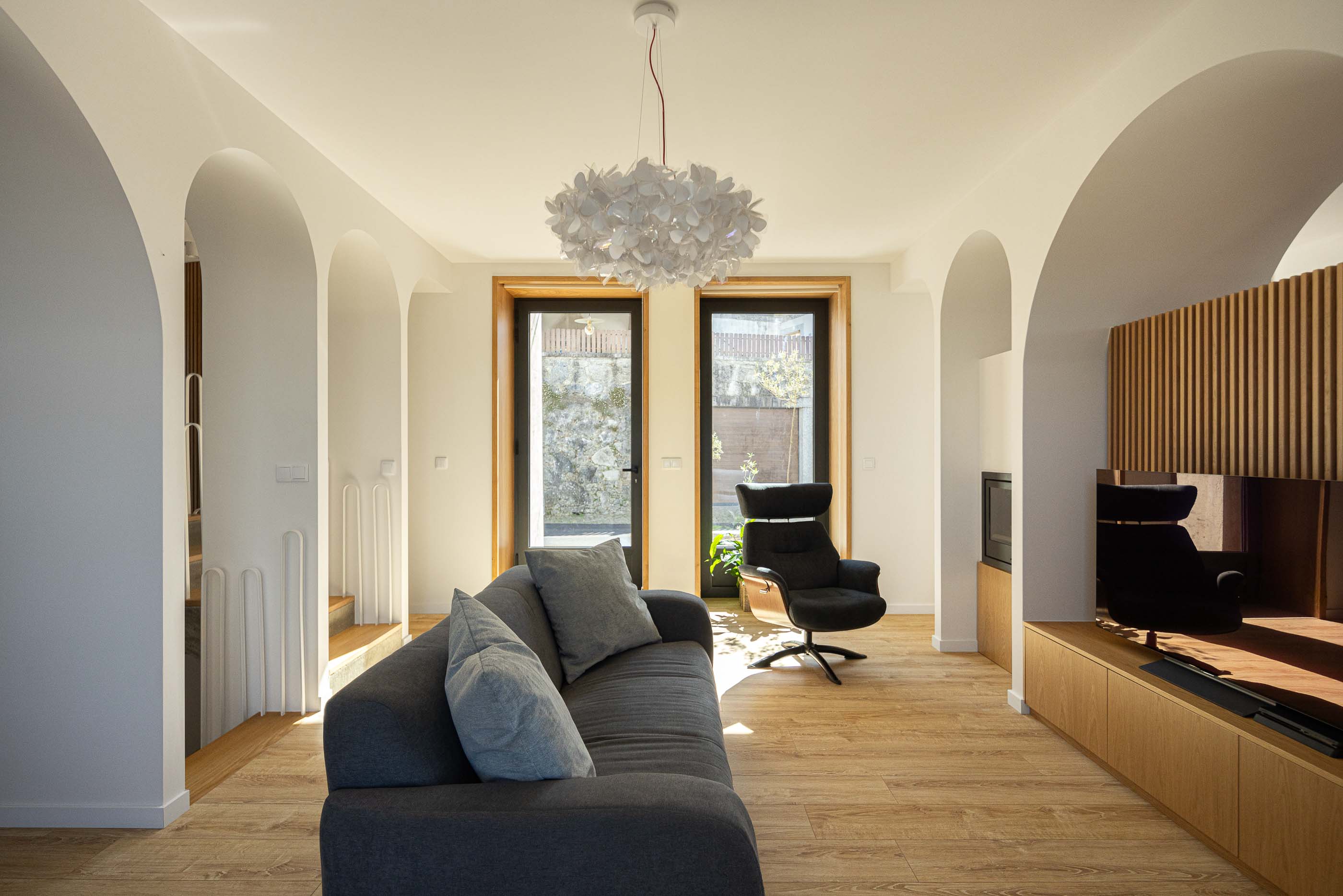 Sala de estar: Sala de estar com sofá cinzento, cadeirão preto, lareira e candeeiro suspenso. — Casa Arco arquitetura Tiago Sousa Arquitecto em Paredes de Coura