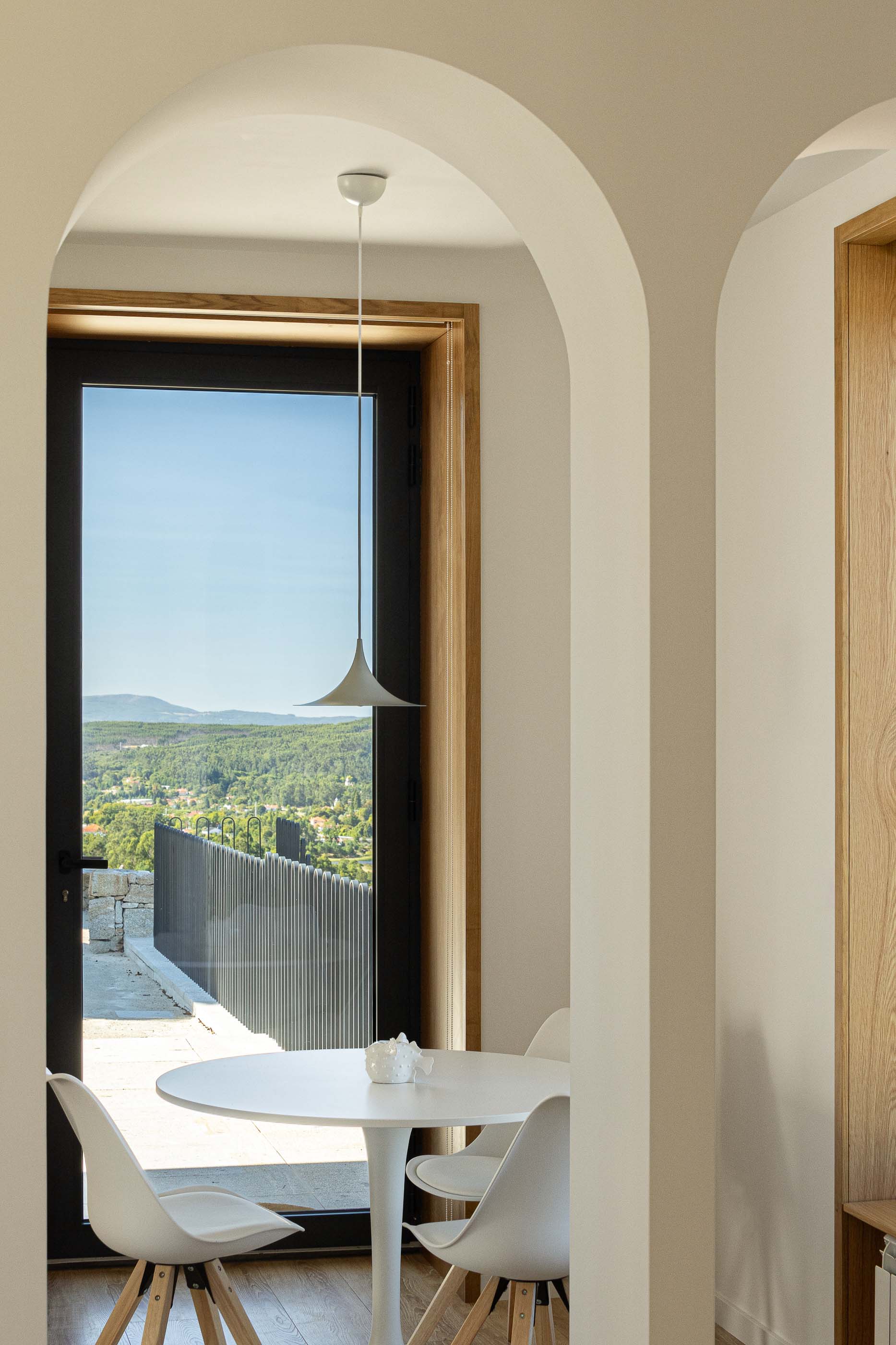 Sala de jantar: Mesa redonda branca com cadeiras e candeeiro suspenso na sala de jantar. — Casa Arco arquitetura Tiago Sousa Arquitecto em Paredes de Coura