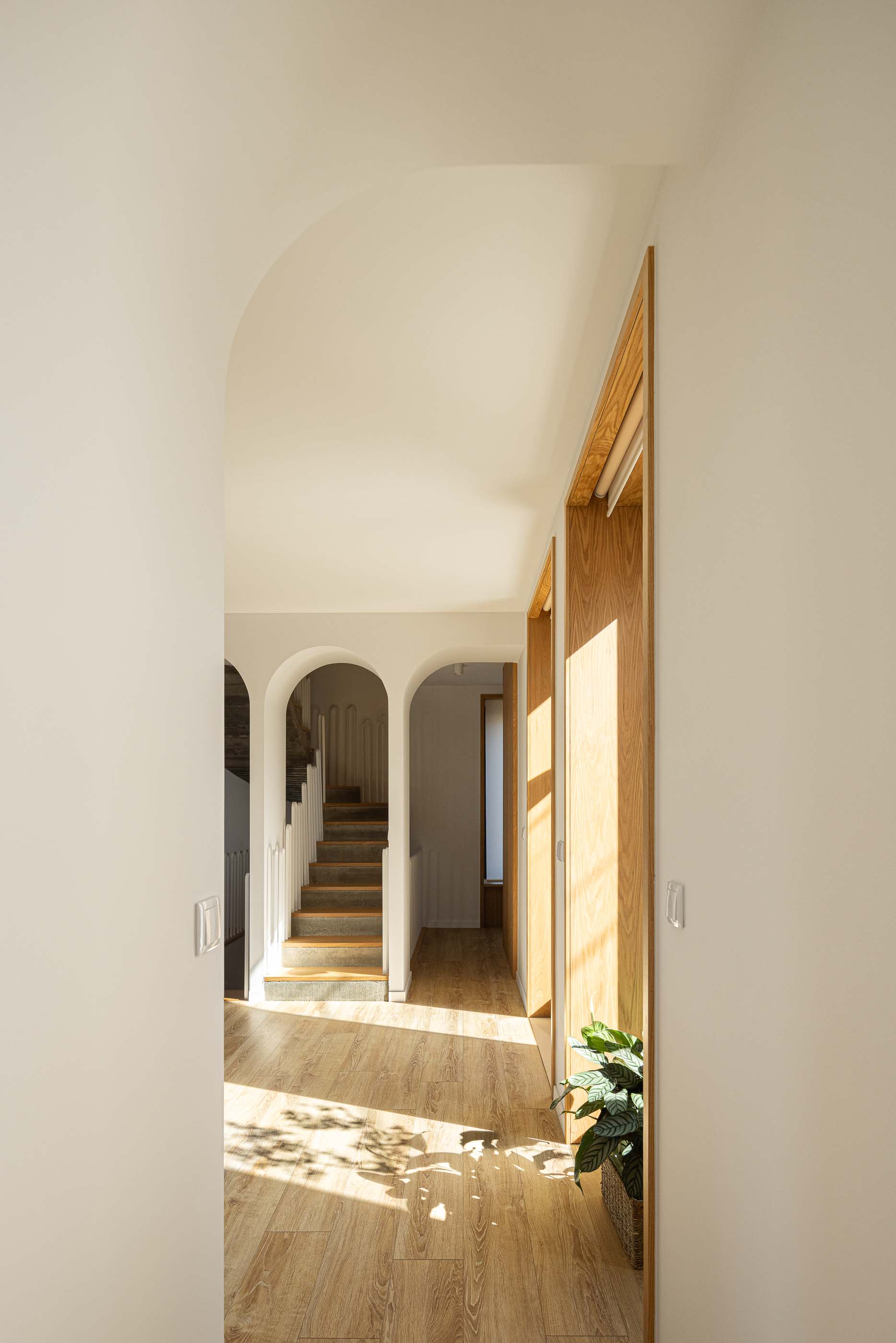 Corredor: Corredor com arcos, pavimento em madeira e porta em madeira. — Casa Arco arquitetura Tiago Sousa Arquitecto em Paredes de Coura