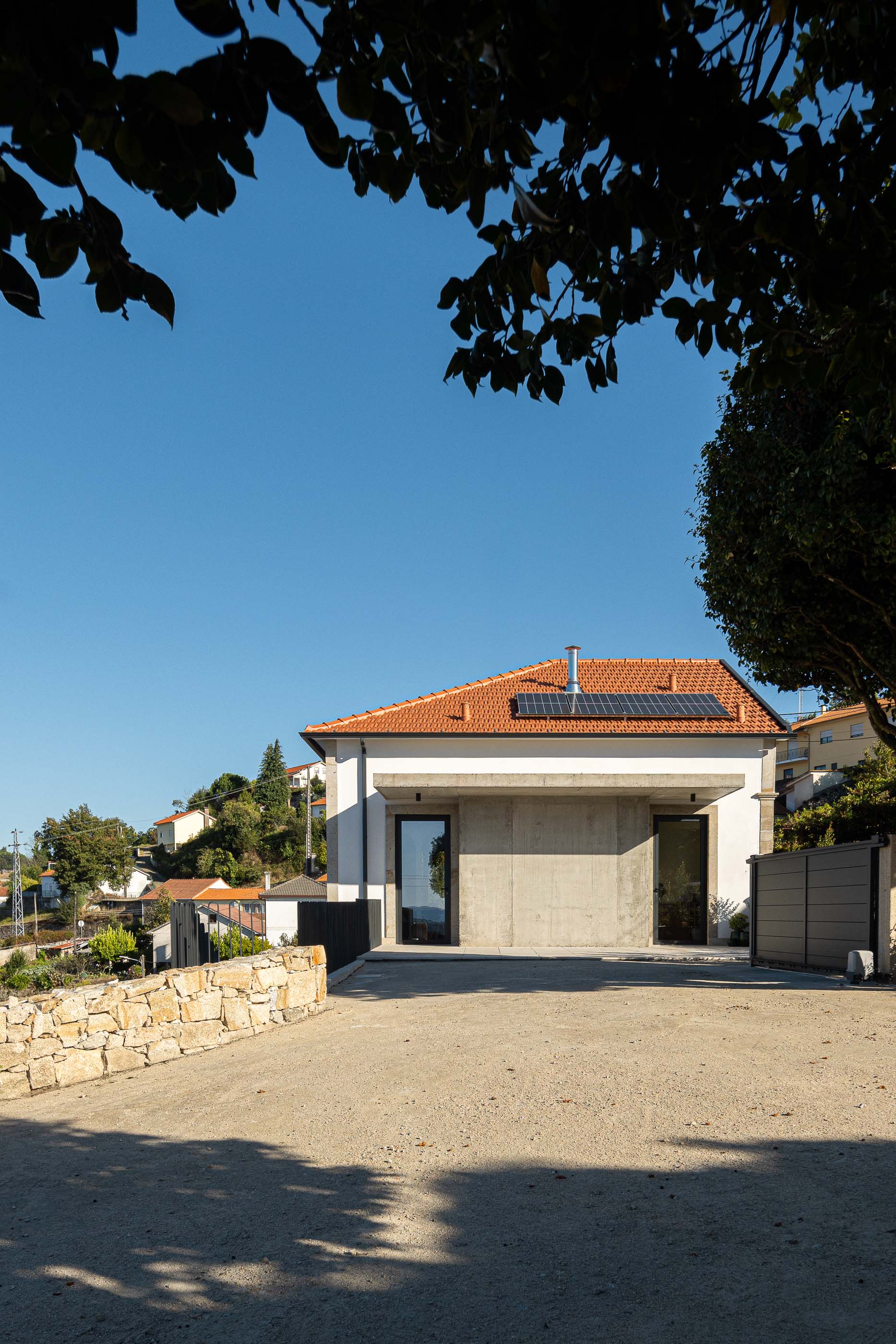 Exterior: Vista da fachada posterior em betão e pedra, com portão metálico. — Casa Arco arquitetura Tiago Sousa Arquitecto em Paredes de Coura
