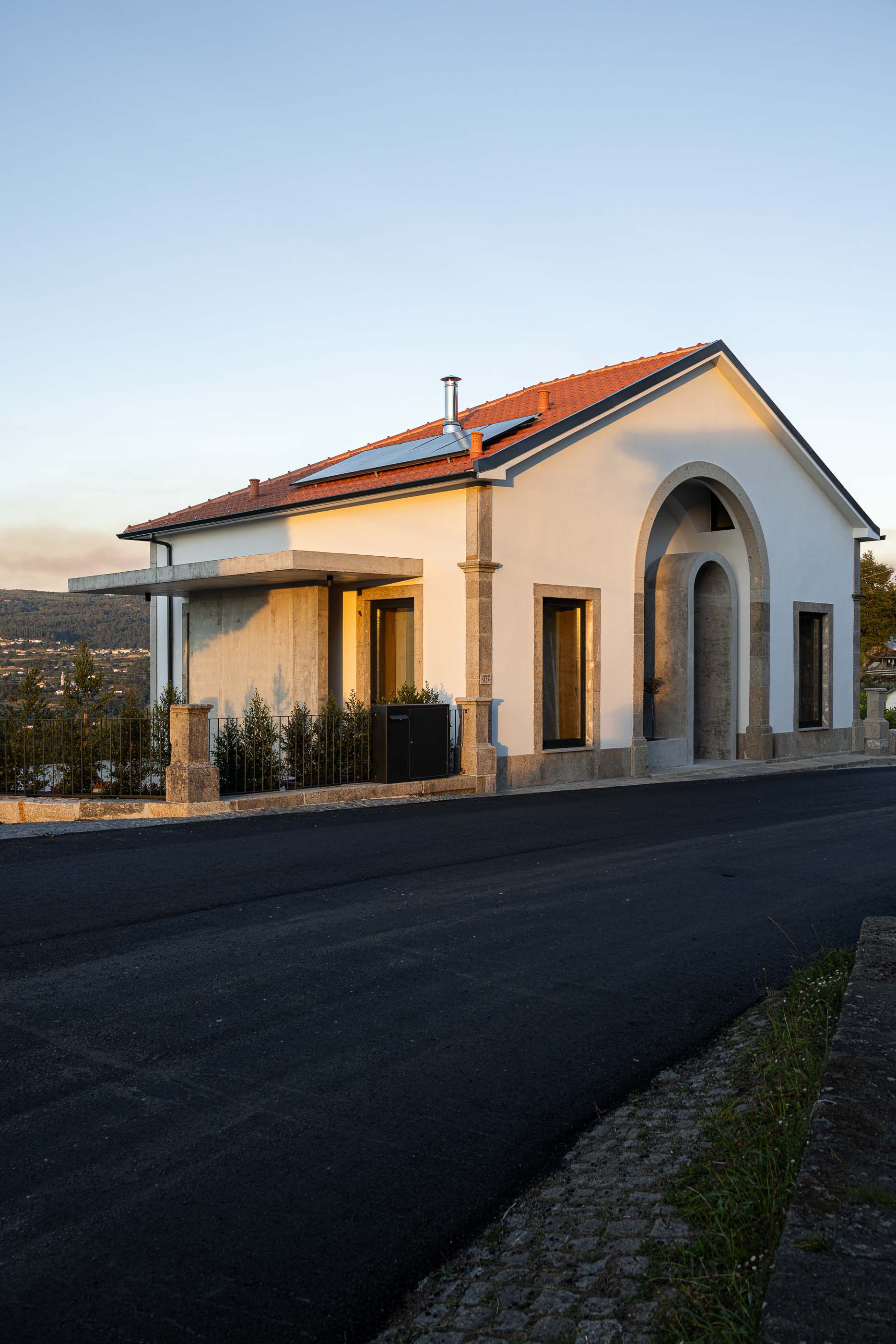 Fachada: Vista da fachada principal da casa com cantaria em granito ao pôr do sol. — Casa Arco arquitetura Tiago Sousa Arquitecto em Paredes de Coura