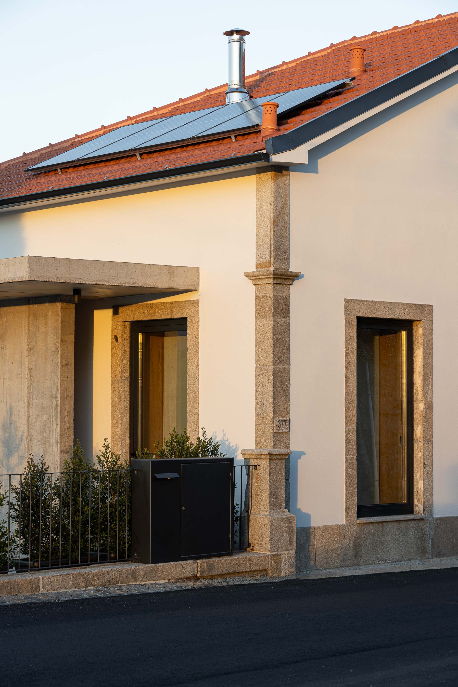 Fachada: Pormenor da fachada com cantaria em granito e painéis solares ao pôr do sol. — Casa Arco arquitetura Tiago Sousa Arquitecto em Paredes de Coura