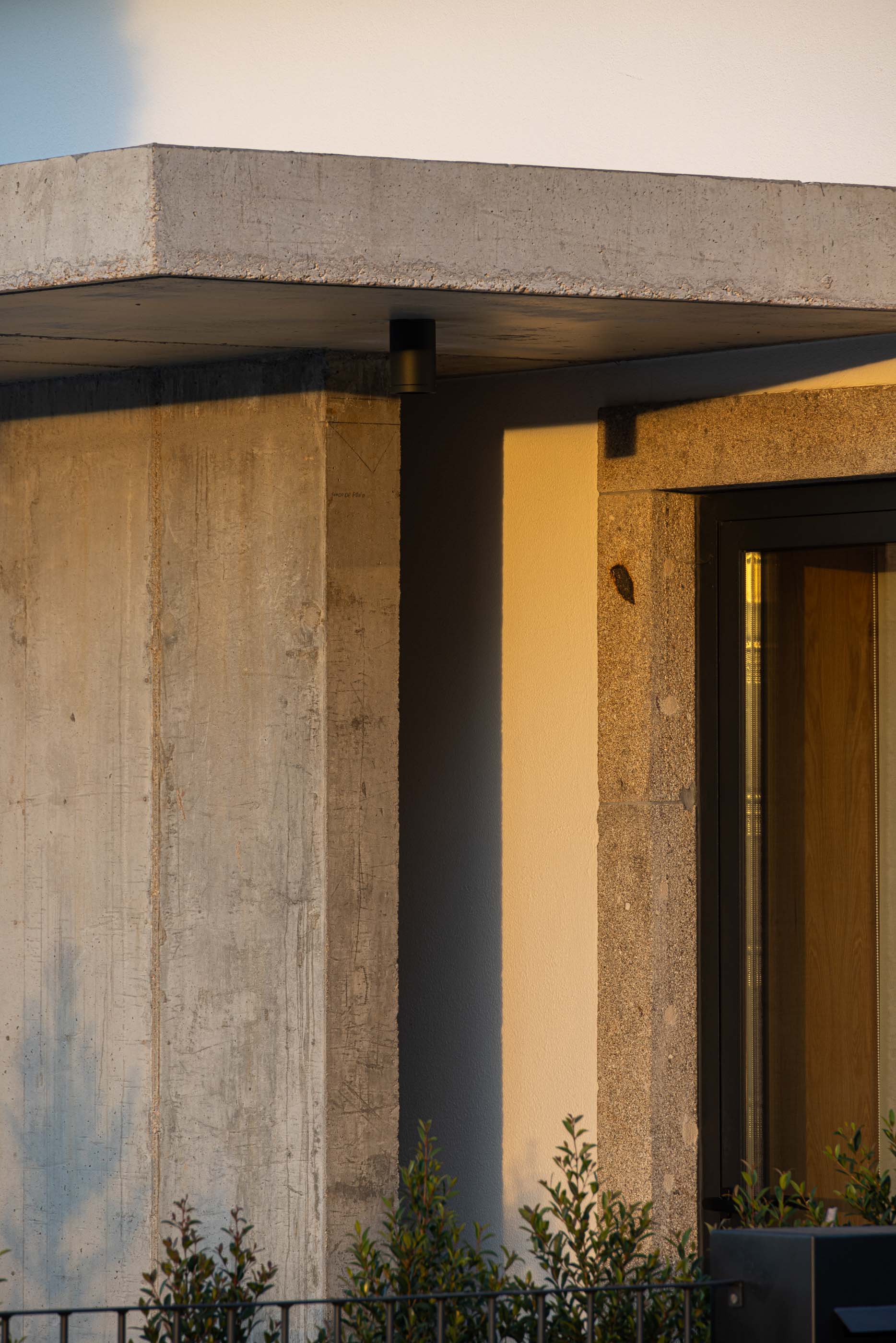 Fachada: Pormenor da fachada em betão e cantaria em granito ao pôr do sol. — Casa Arco arquitetura Tiago Sousa Arquitecto em Paredes de Coura