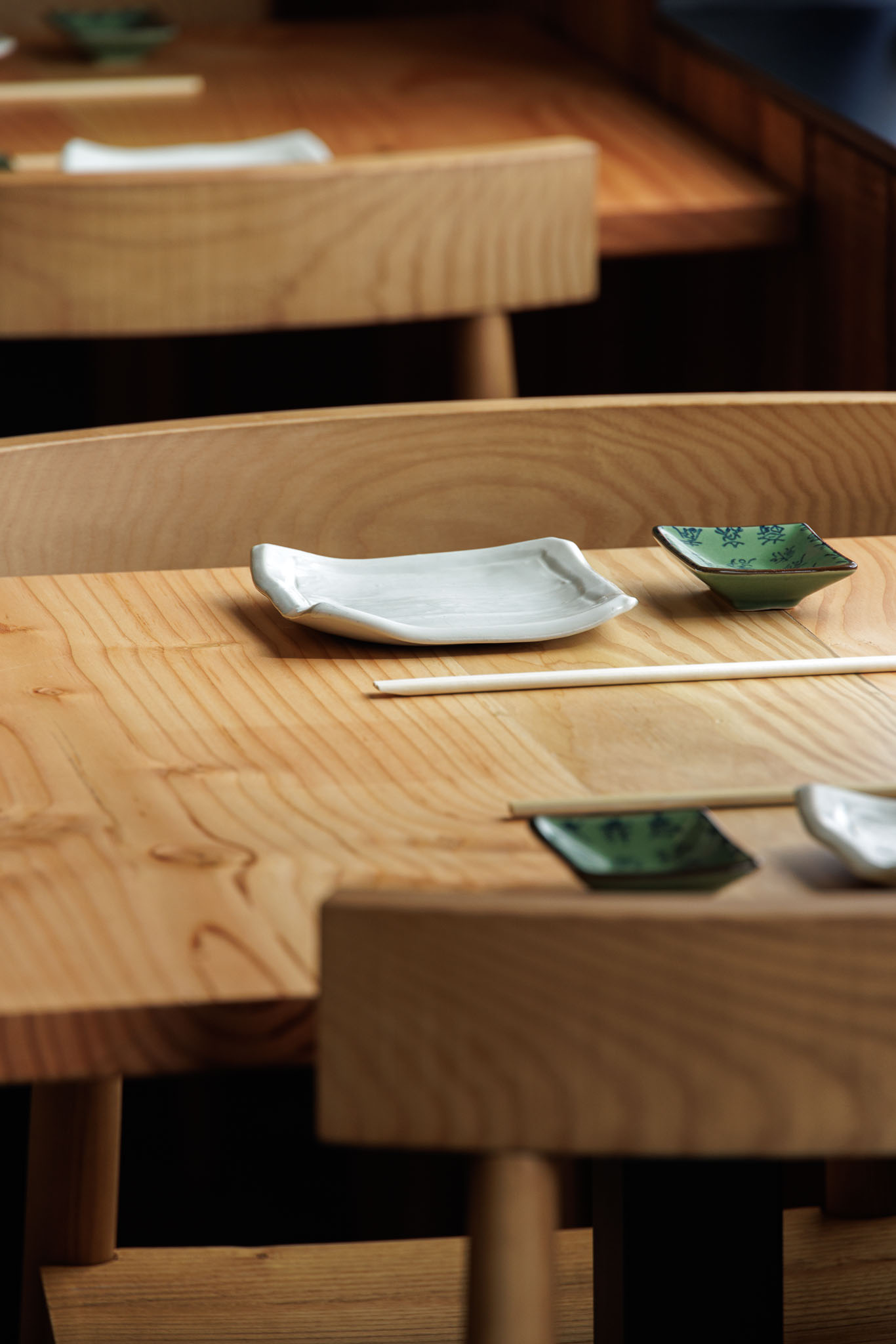 Detalhe da mesa: Pratos de cerâmica branca e verde, pauzinhos sobre mesa de madeira clara. — Restaurante Izakaya Matsuri arquitetura Ferreira Arquitetos em Aveiro