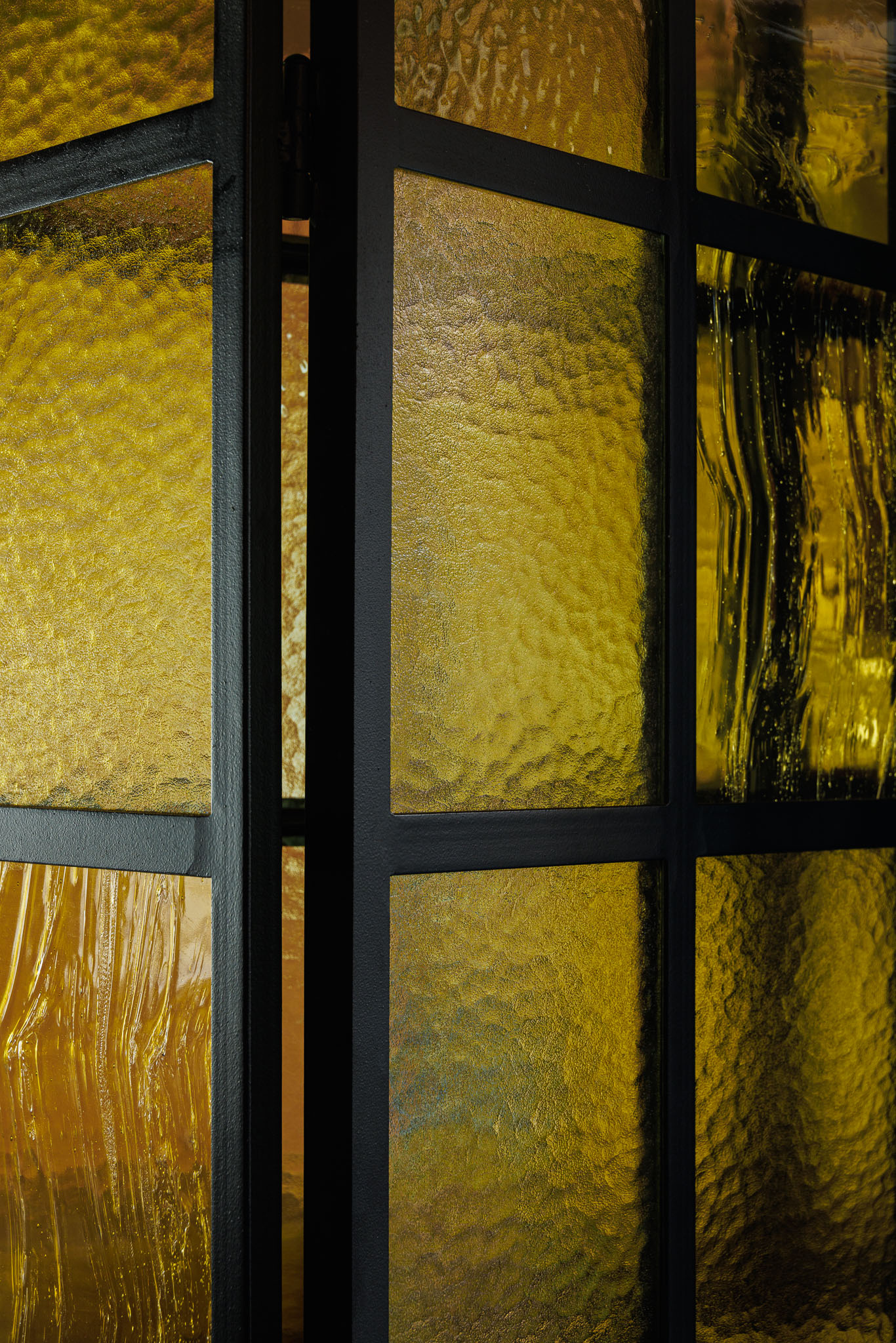 Detalhe da divisória: Vidro texturado amarelo em estrutura metálica preta, com reflexos de luz. — Restaurante Izakaya Matsuri arquitetura Ferreira Arquitetos em Aveiro