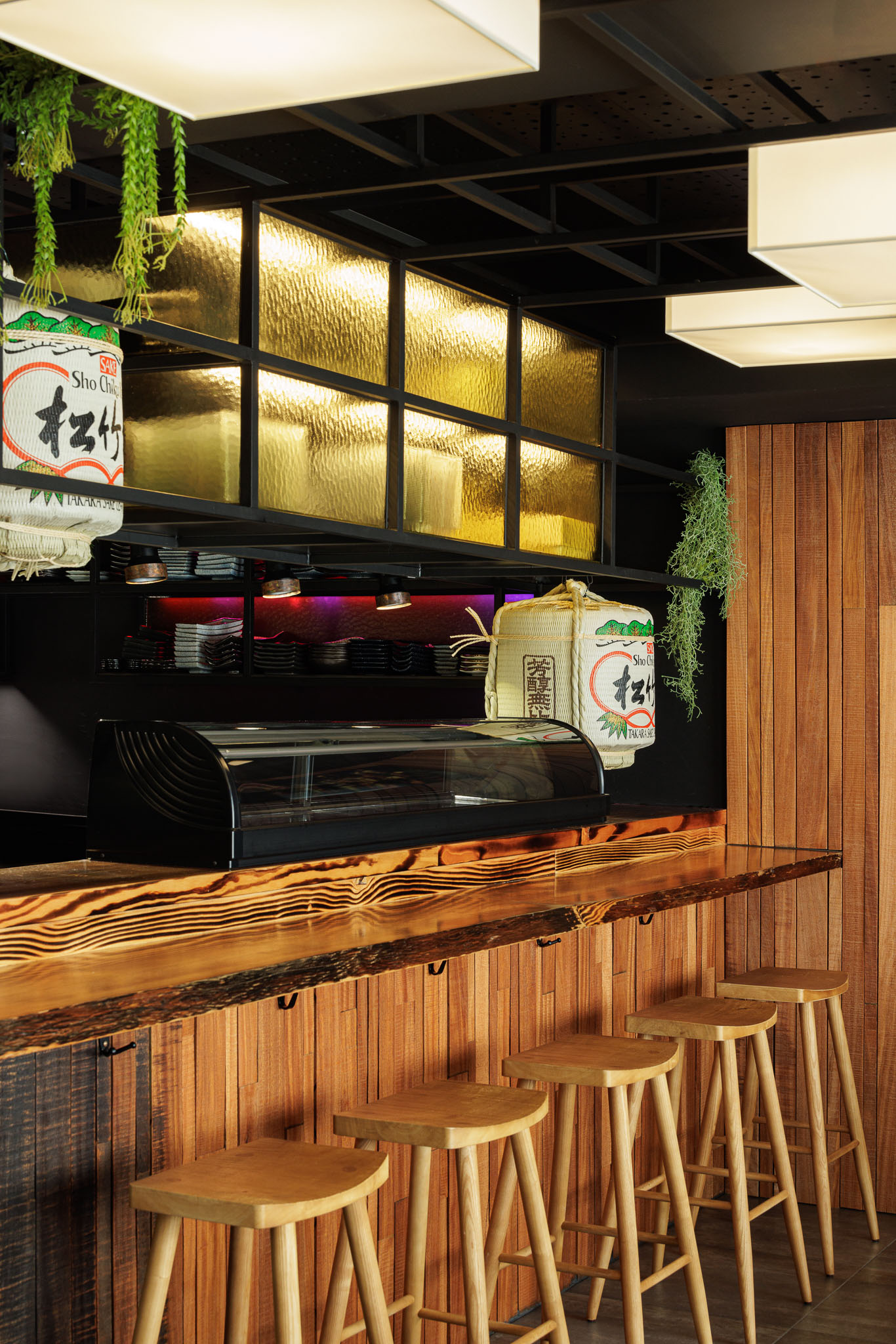 Balcão: Balcão em madeira rústica, revestimento em madeira, bancos altos, prateleiras com garrafas e decoração japonesa. — Restaurante Izakaya Matsuri arquitetura Ferreira Arquitetos em Aveiro