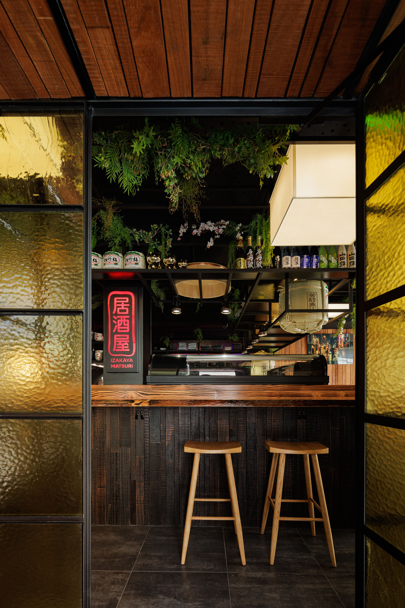 Balcão: Balcão em madeira rústica, bancos altos, divisória em vidro texturado amarelo e decoração japonesa. — Restaurante Izakaya Matsuri arquitetura Ferreira Arquitetos em Aveiro