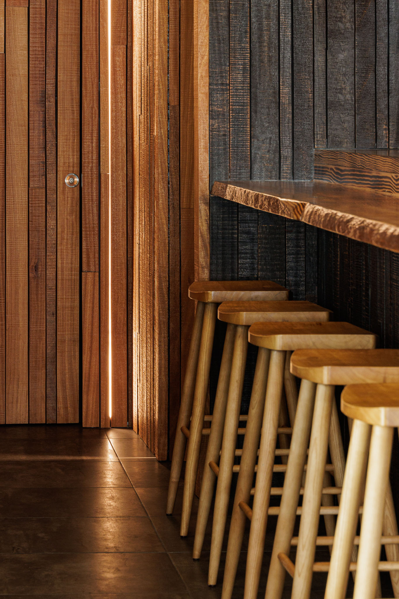 Balcão: Detalhe do balcão em madeira rústica, bancos altos e porta em madeira com iluminação. — Restaurante Izakaya Matsuri arquitetura Ferreira Arquitetos em Aveiro