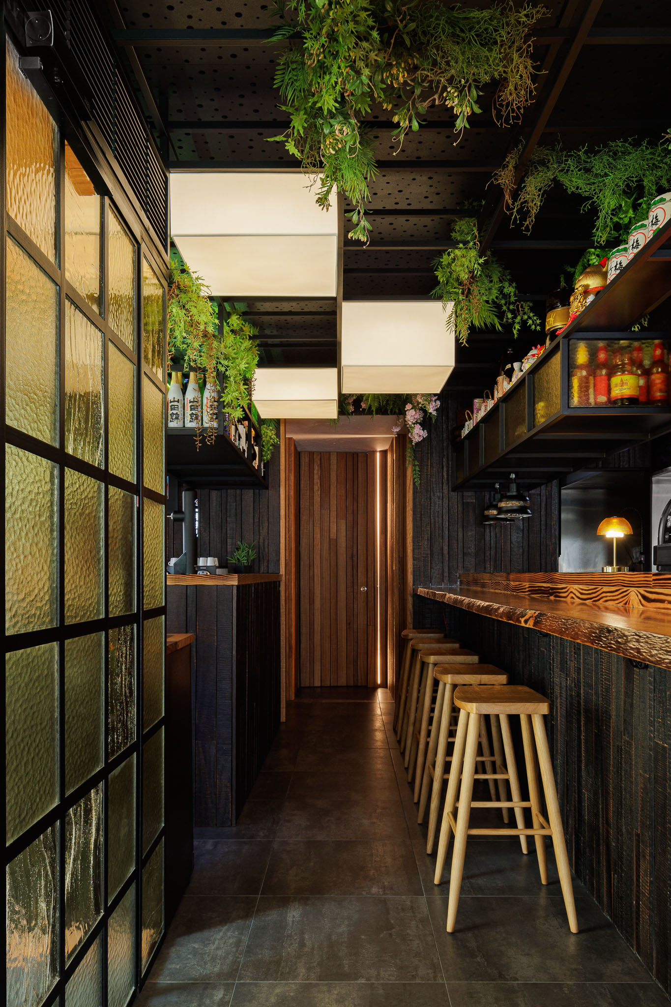 Corredor: Balcão, bancos altos, divisória de vidro texturado amarelo e porta em madeira iluminada. — Restaurante Izakaya Matsuri arquitetura Ferreira Arquitetos em Aveiro