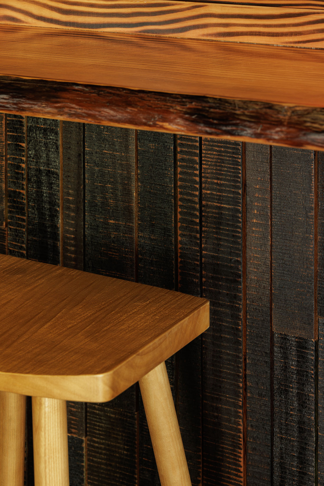 Balcão: Detalhe do balcão em madeira rústica, revestimento em madeira escura e banco alto de madeira. — Restaurante Izakaya Matsuri arquitetura Ferreira Arquitetos em Aveiro