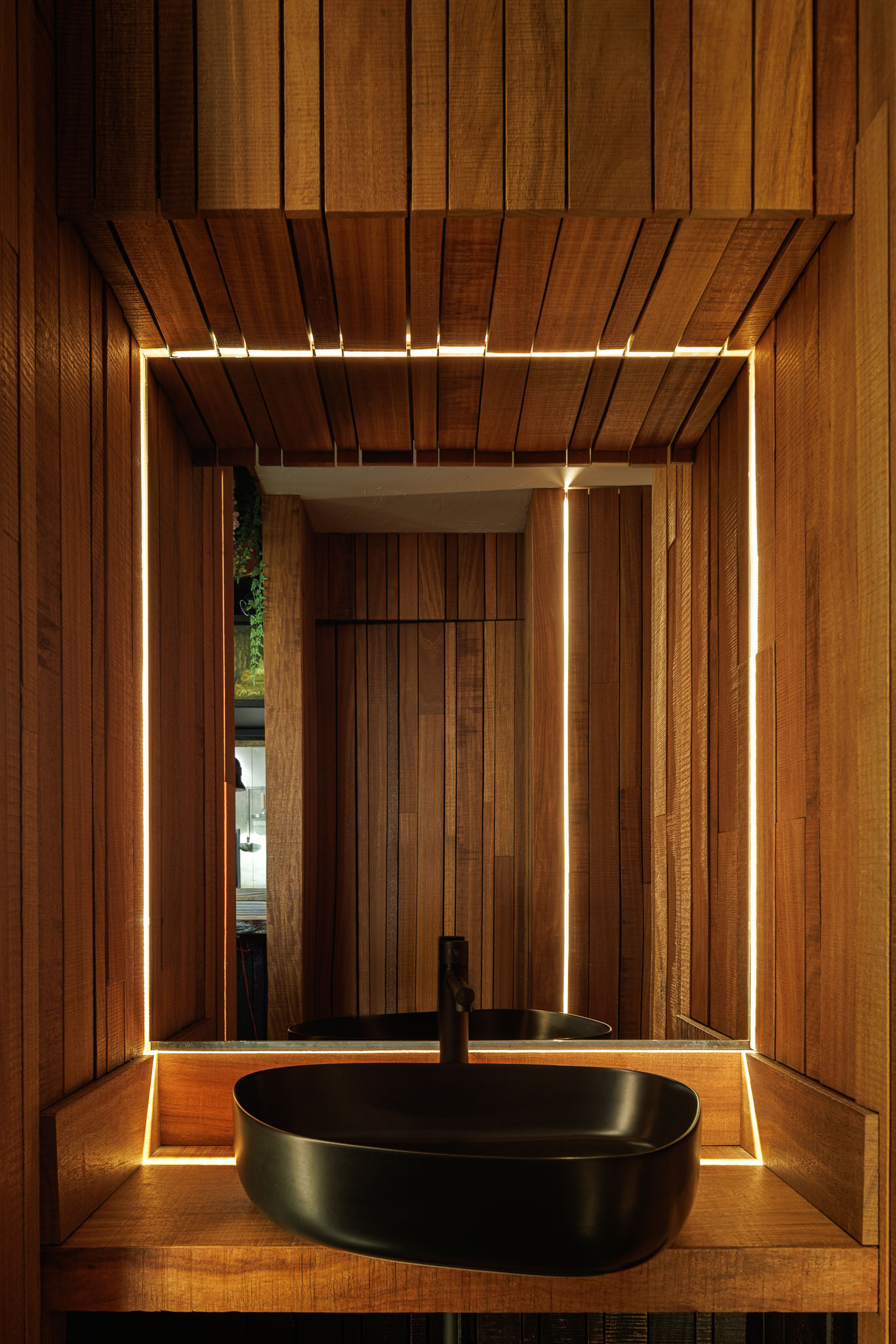 Casa de banho: Espelho iluminado, lavatório preto sobre bancada de madeira e revestimento em madeira. — Restaurante Izakaya Matsuri arquitetura Ferreira Arquitetos em Aveiro