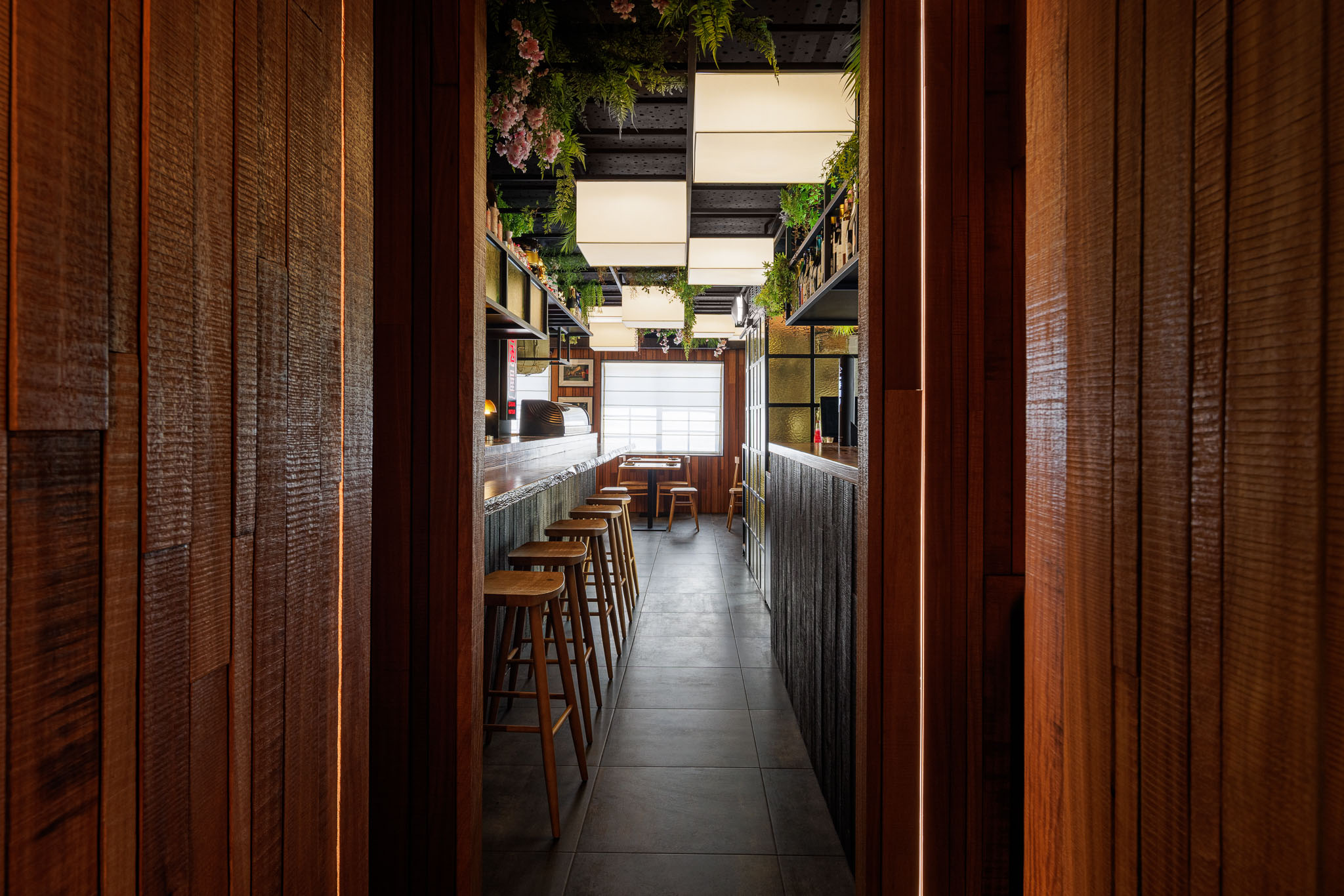 Corredor: Vista do corredor com balcão, bancos altos e iluminação embutida na madeira. — Restaurante Izakaya Matsuri arquitetura Ferreira Arquitetos em Aveiro