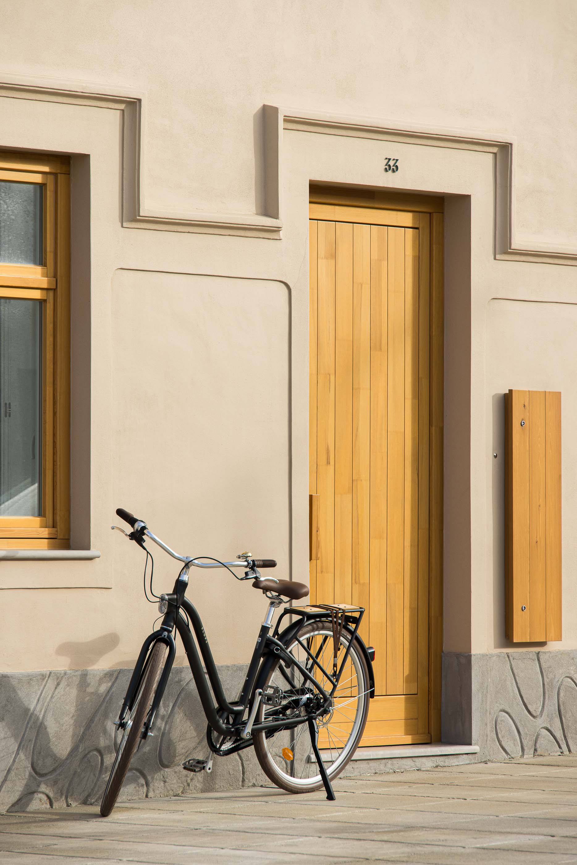 Entrada: Fachada bege com porta de madeira clara, bicicleta preta encostada. Detalhes arquitetónicos clássicos. — Casa Clara arquitetura M2Senos Arquitectos em Ílhavo