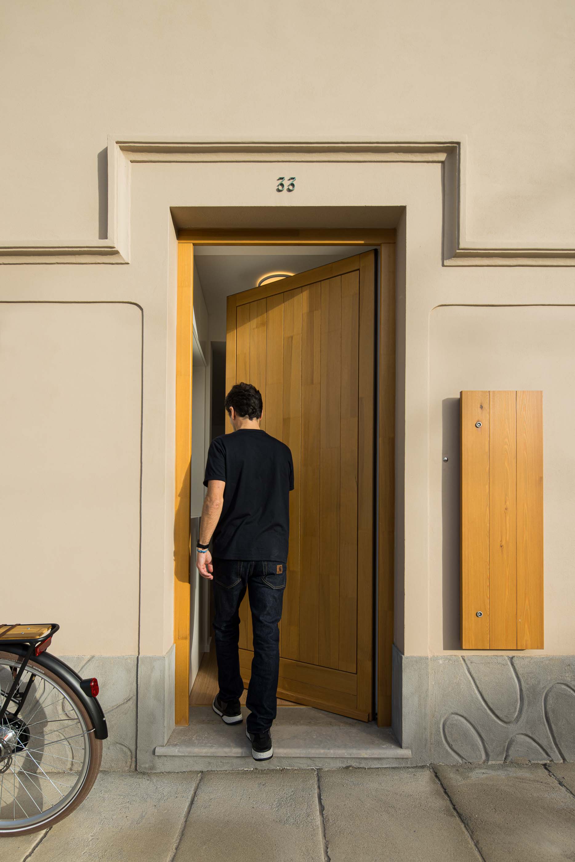 Entrada: Homem a entrar pela porta de madeira clara. Fachada bege com detalhes clássicos e número 33. — Casa Clara arquitetura M2Senos Arquitectos em Ílhavo