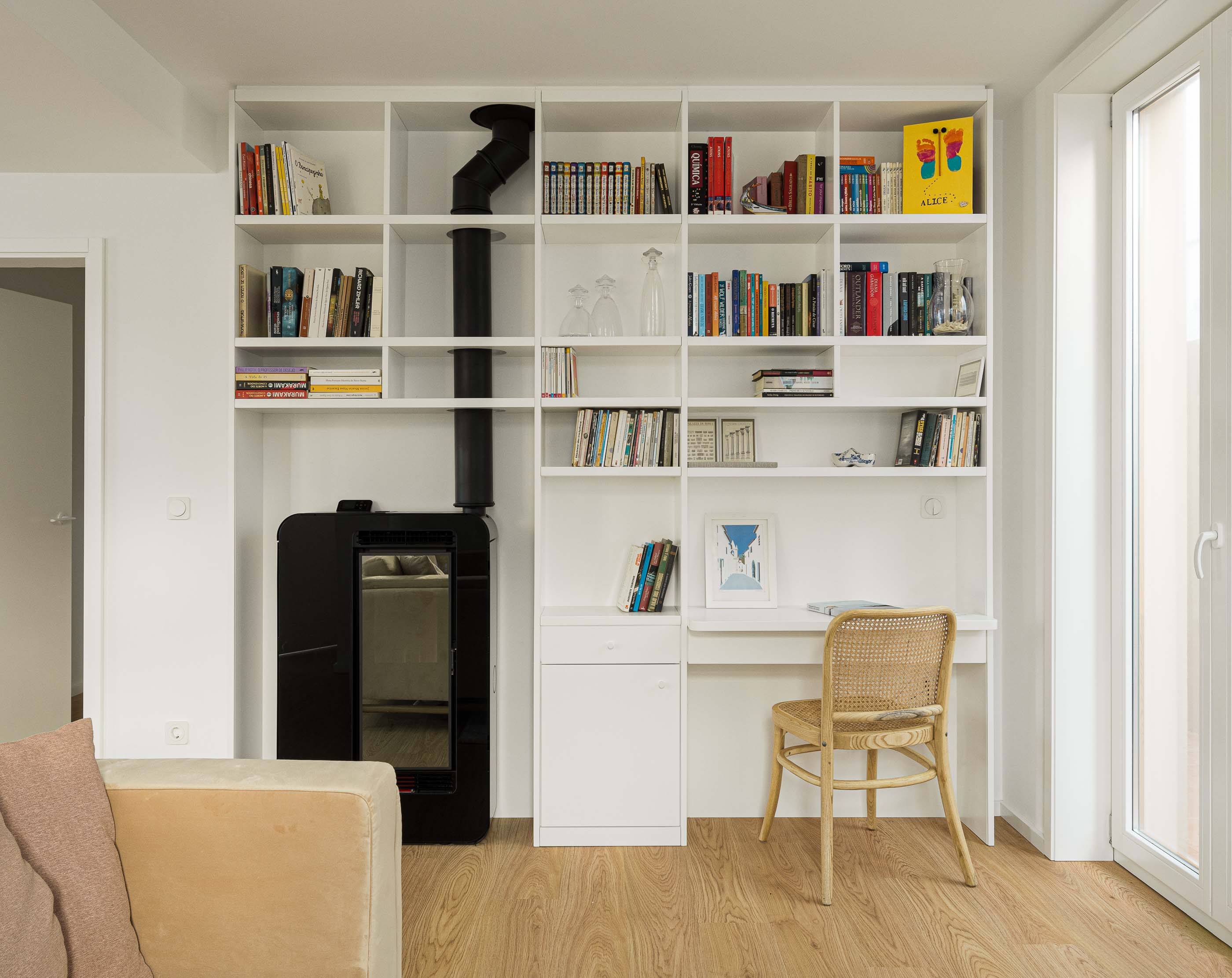 Sala de estar/Escritório: Estante branca com lareira a pellets, secretária e cadeira de palhinha. Sofá bege. — Casa Clara arquitetura M2Senos Arquitectos em Ílhavo