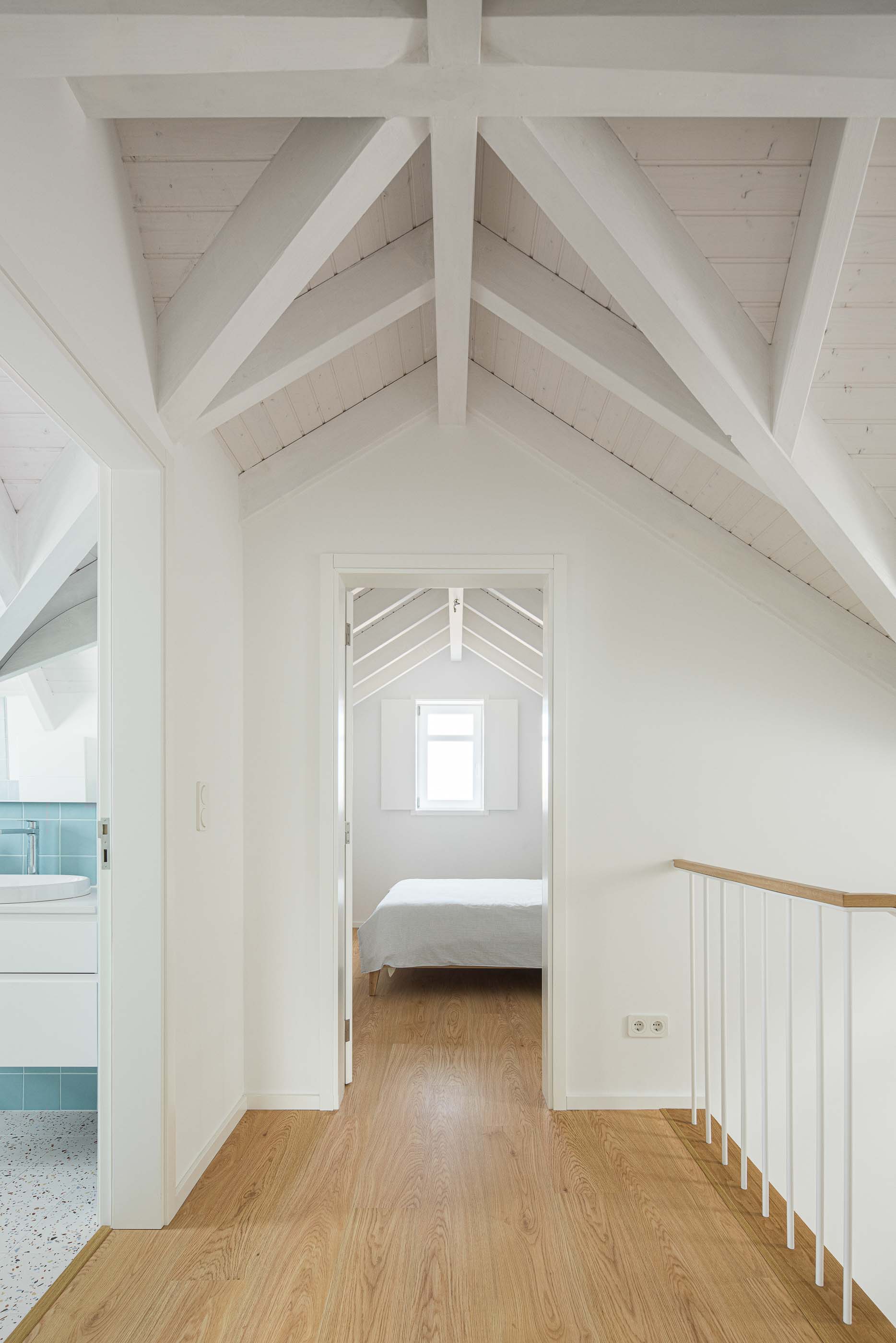 Corredor: Corredor no sótão com pavimento de madeira, paredes brancas e acesso a casa de banho e quarto. — Casa Clara arquitetura M2Senos Arquitectos em Ílhavo