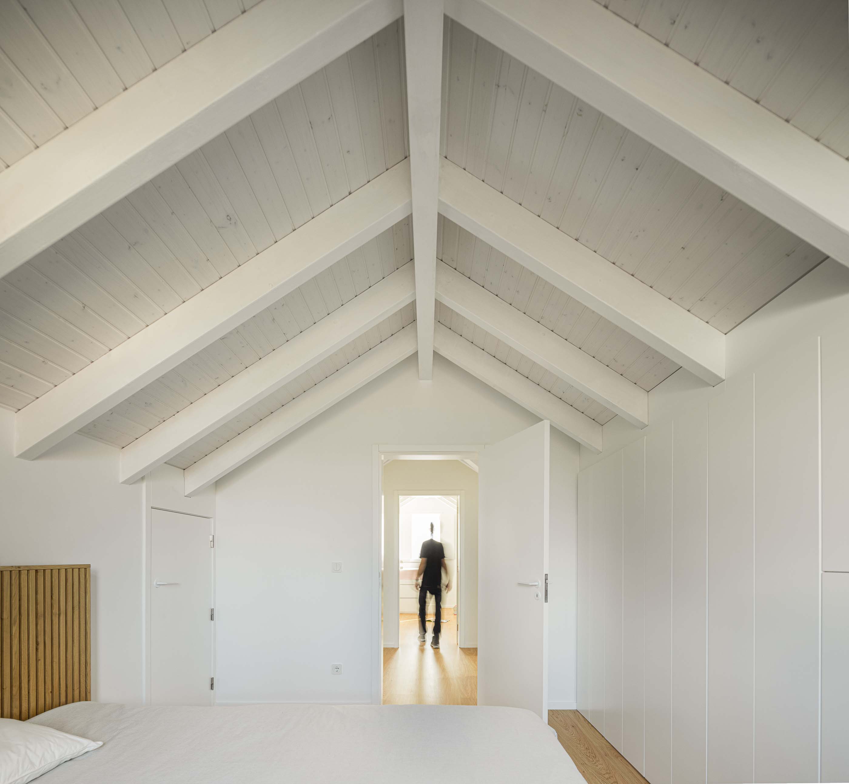 Quarto: Quarto no sótão com cama de casal, roupeiro branco e teto com vigas de madeira pintadas de branco. — Casa Clara arquitetura M2Senos Arquitectos em Ílhavo