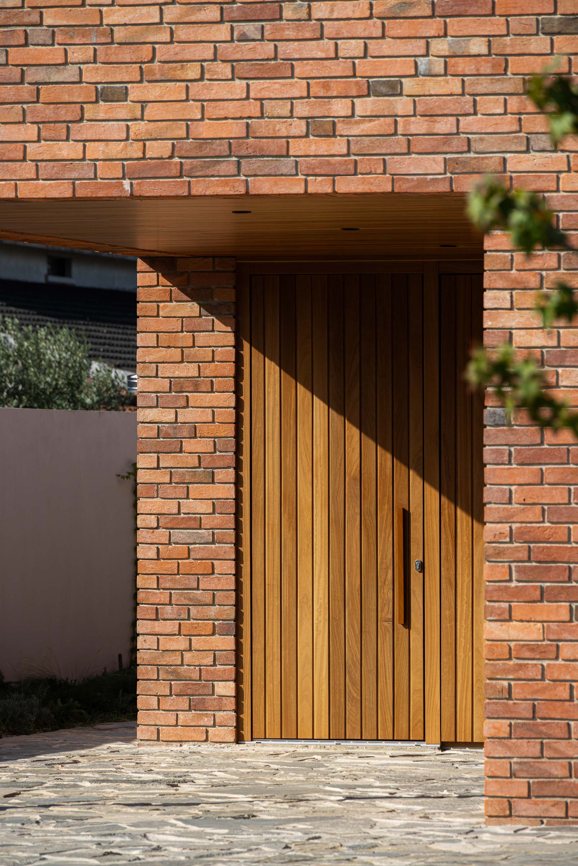 Entrada: Detalhe da porta principal em madeira com puxador vertical, emoldurada por tijolo rústico. — Casa na Lameira arquitetura João Pedro Pedrosa - Arquitectos em Fátima