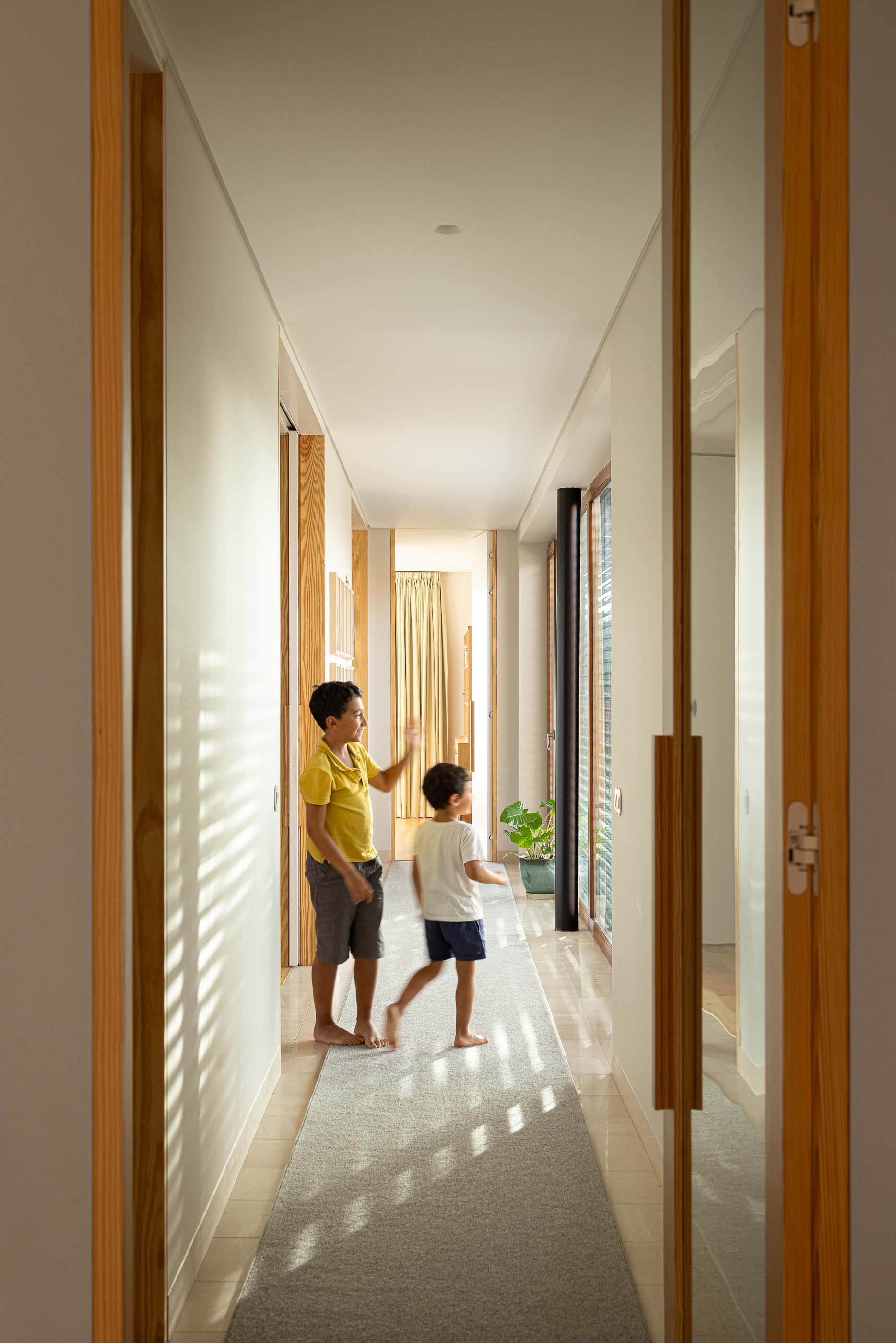 Corredor: Crianças no corredor com alcatifa, portas em madeira e luz natural. — Casa na Lameira arquitetura João Pedro Pedrosa - Arquitectos em Fátima