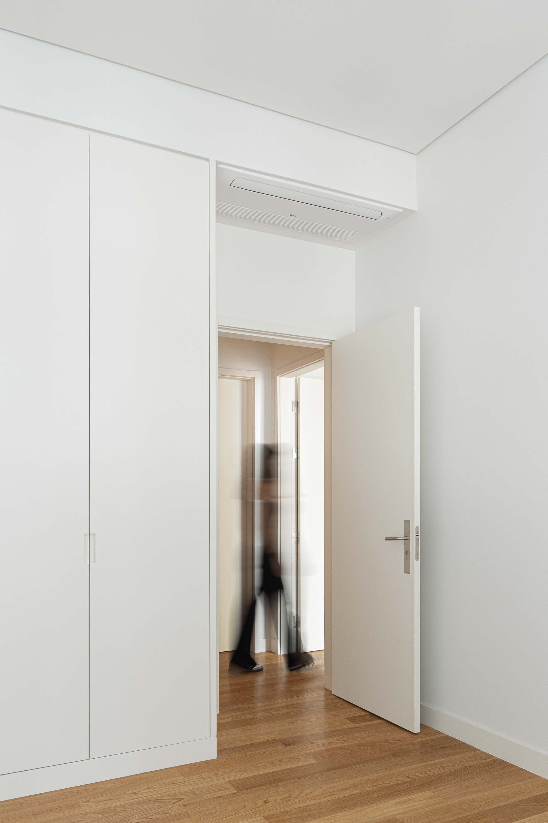 Quarto com pavimento em madeira, roupeiro branco embutido e porta aberta para outro espaço. — António Enes 13 arquitetura Pedro Carrilho Arquitectos em Lisboa