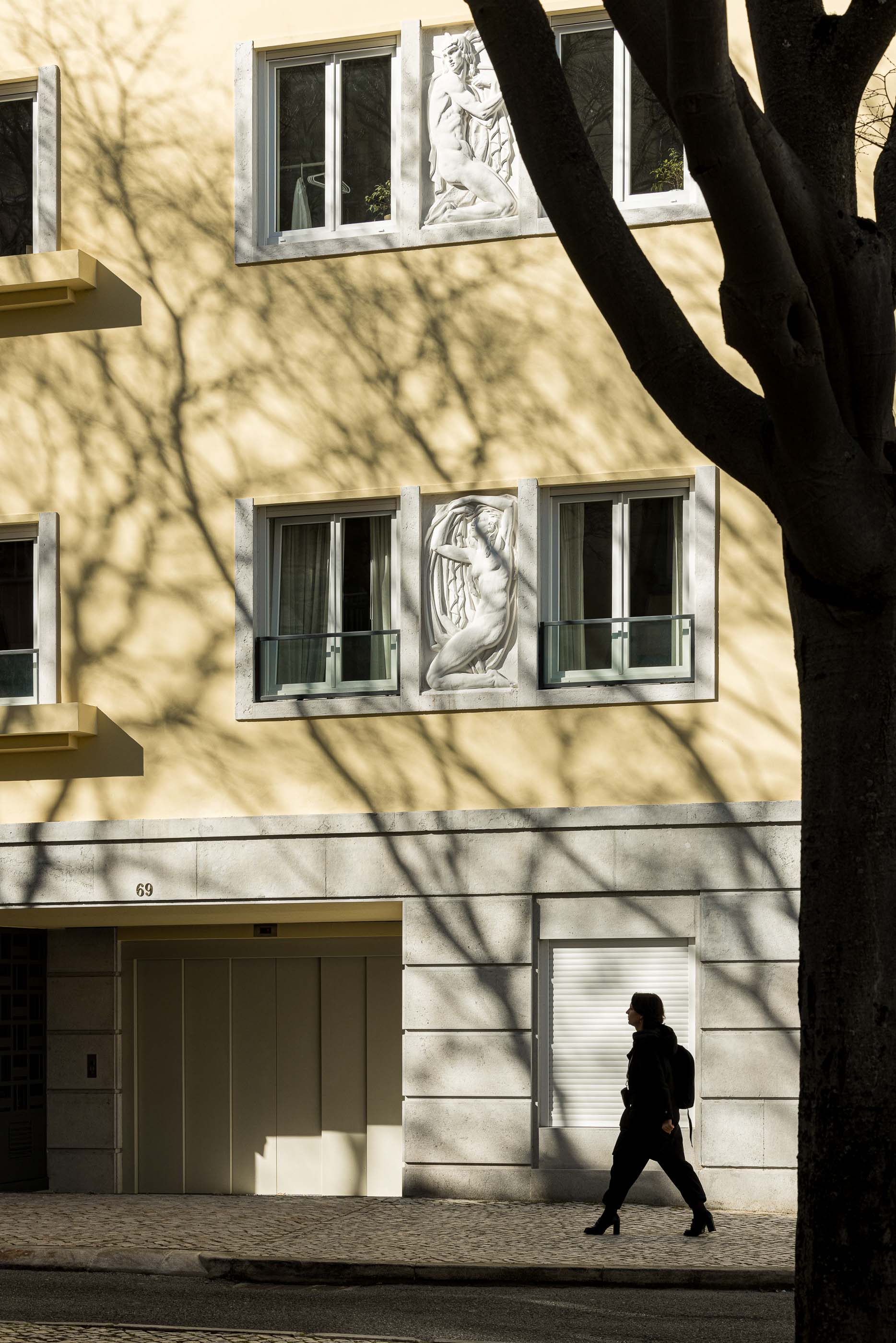 Exterior do edifício com fachada amarela e esculturas nas janelas. — António Enes 13 arquitetura Pedro Carrilho Arquitectos em Lisboa