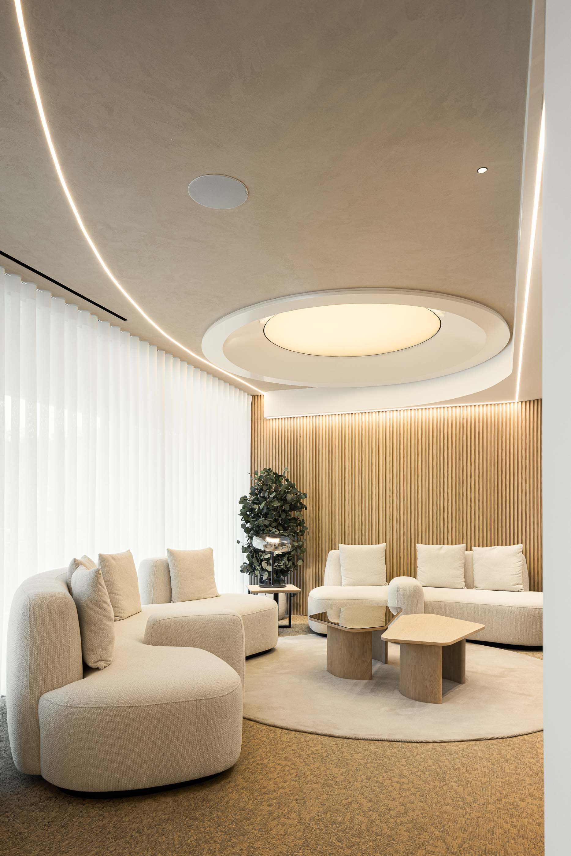 Sala de Espera: Sofás curvos em tecido bouclé, mesas de apoio em madeira clara, alcatifa redonda e cortinas brancas translúcidas. — YOU – Clínica Dentária arquitetura Radian Contemporary Architecture em Malveira